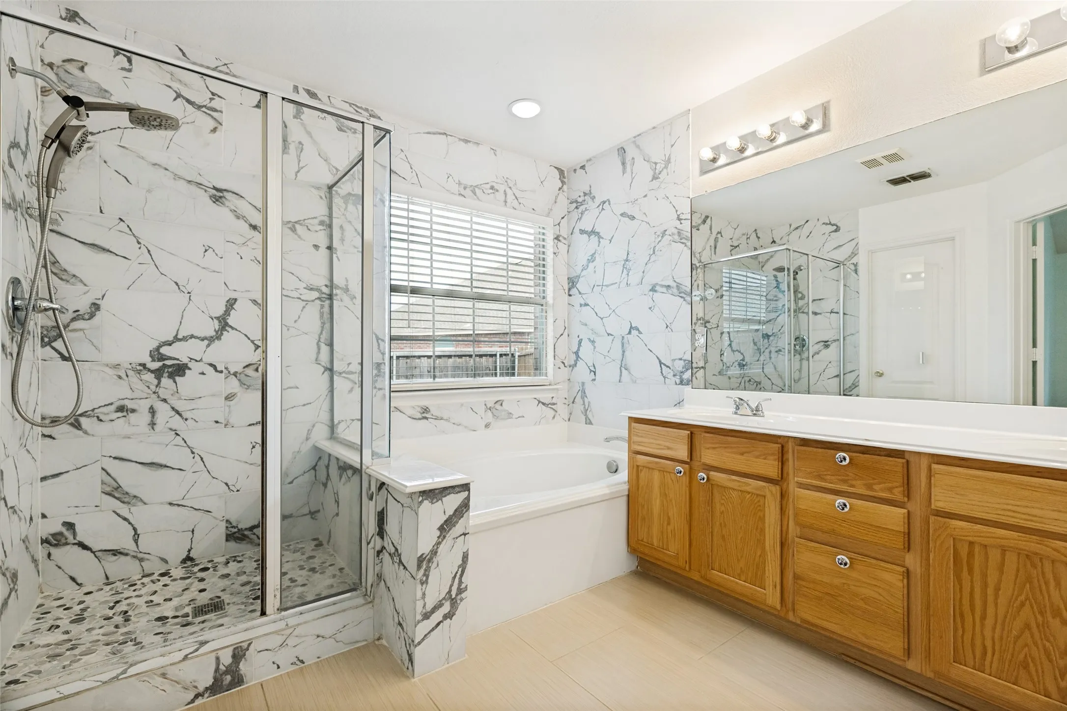 Enclosed glass shower with pebble-finish flooring, white tiled walls, a separate soaking tub, and a double vanity with wood cabinetry