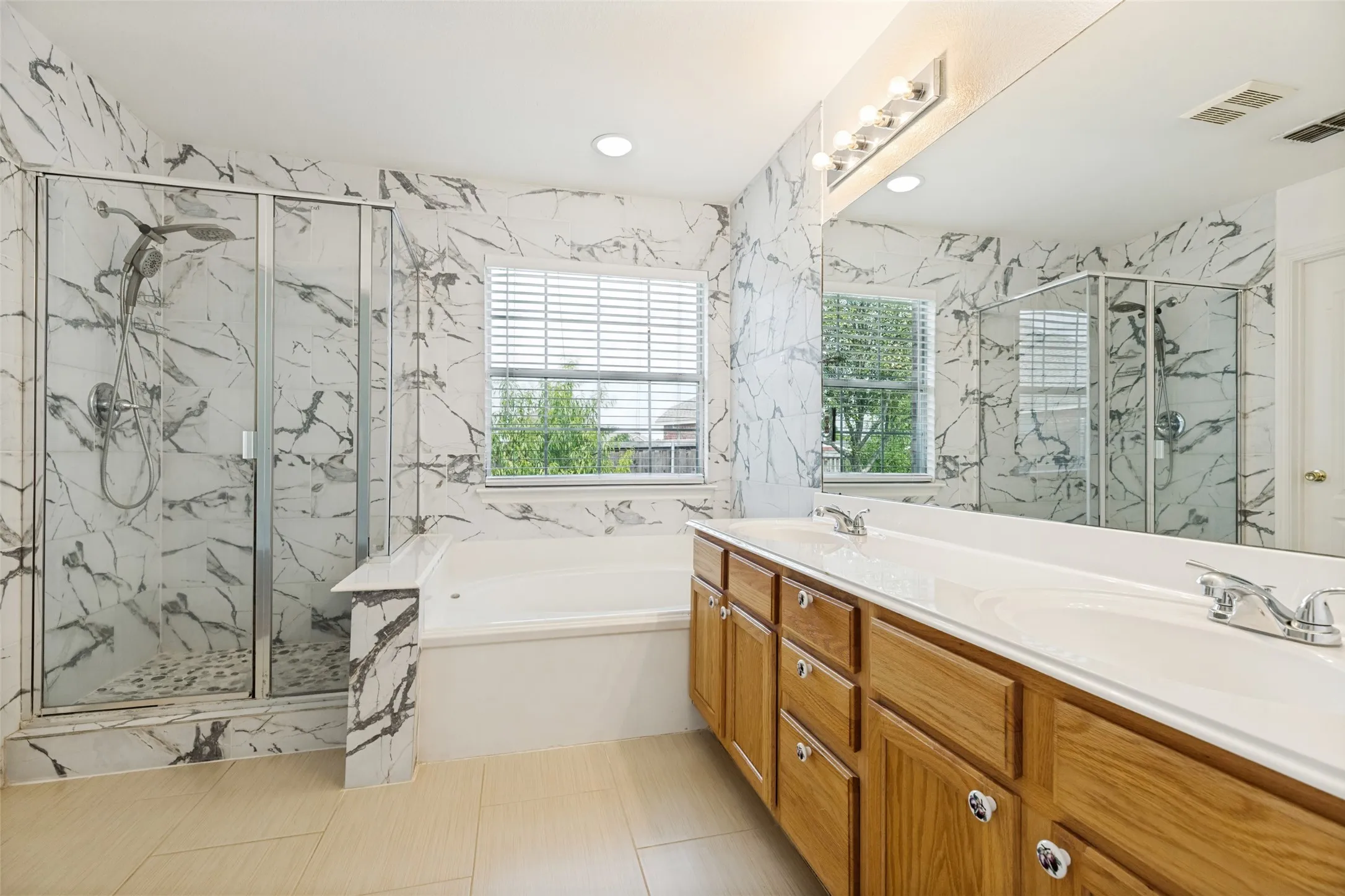Spacious bathroom featuring a dual vanity, polished chrome fixtures, integrated soaking tub, and a separate glass-enclosed shower with a handheld spray