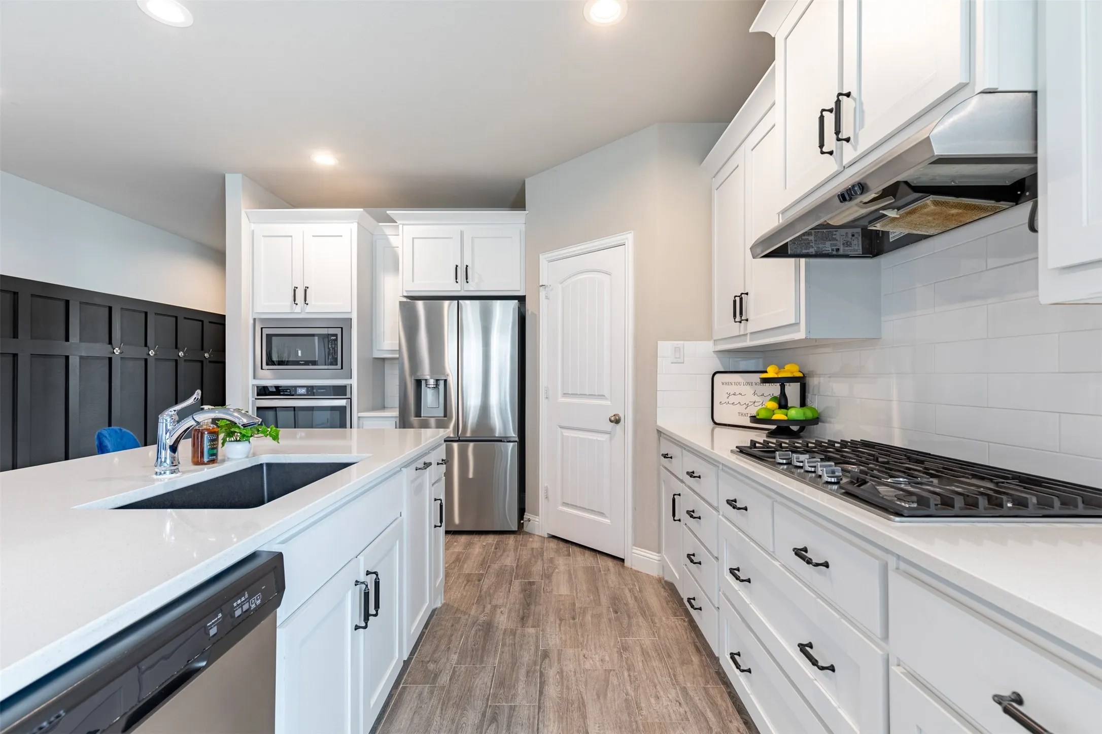 Well-appointed kitchen workspace featuring a farmhouse sink, 5-burner cooktop, ample cabinetry, walk-in pantry, refrigerator, and built-in oven with microwave.