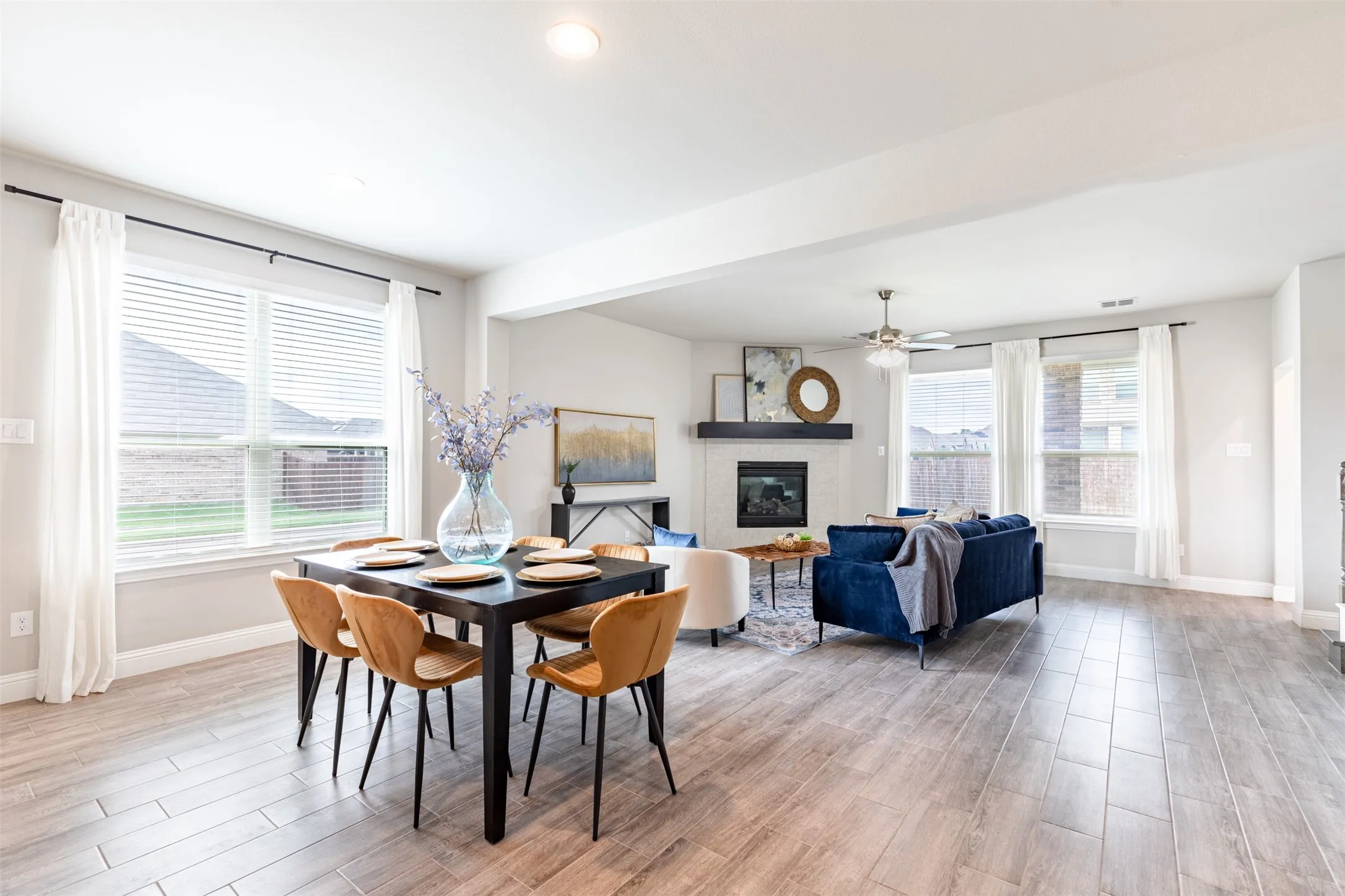 Open-concept eat-in kitchen and living room filled with natural light, featuring a gas fireplace with log insert and ceiling fan for comfortable everyday living.