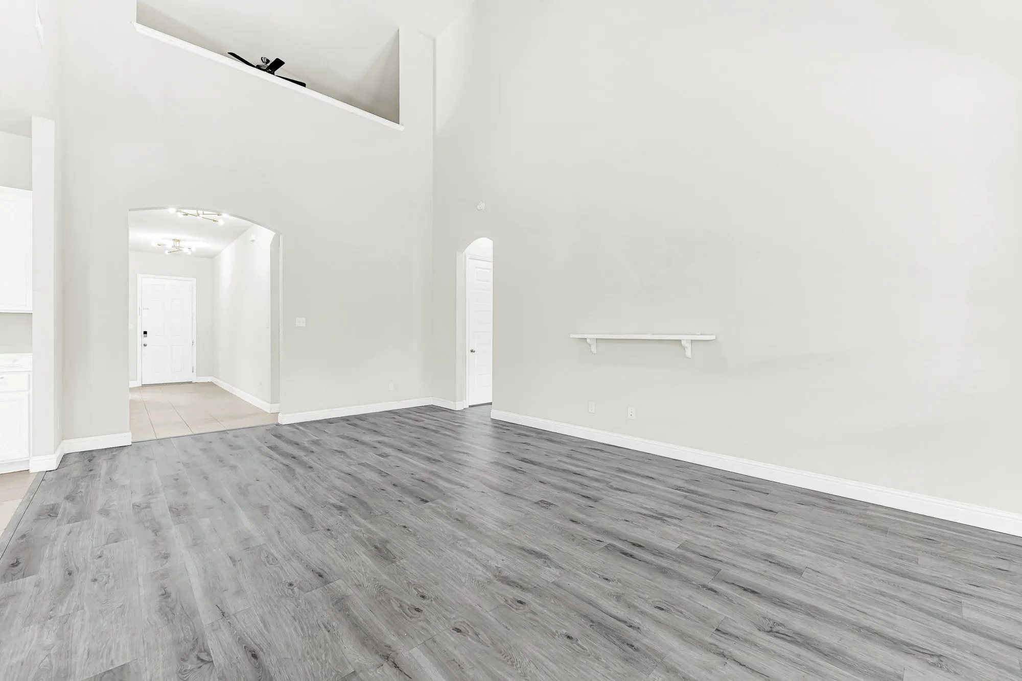 A soaring two-story ceiling and dramatic arched entryways create a grand sense of vertical space while allowing light to bounce freely across cool-toned flooring. You can easily picture wrapping up a long day with a cozy movie night under the lofty, open airy layout.
