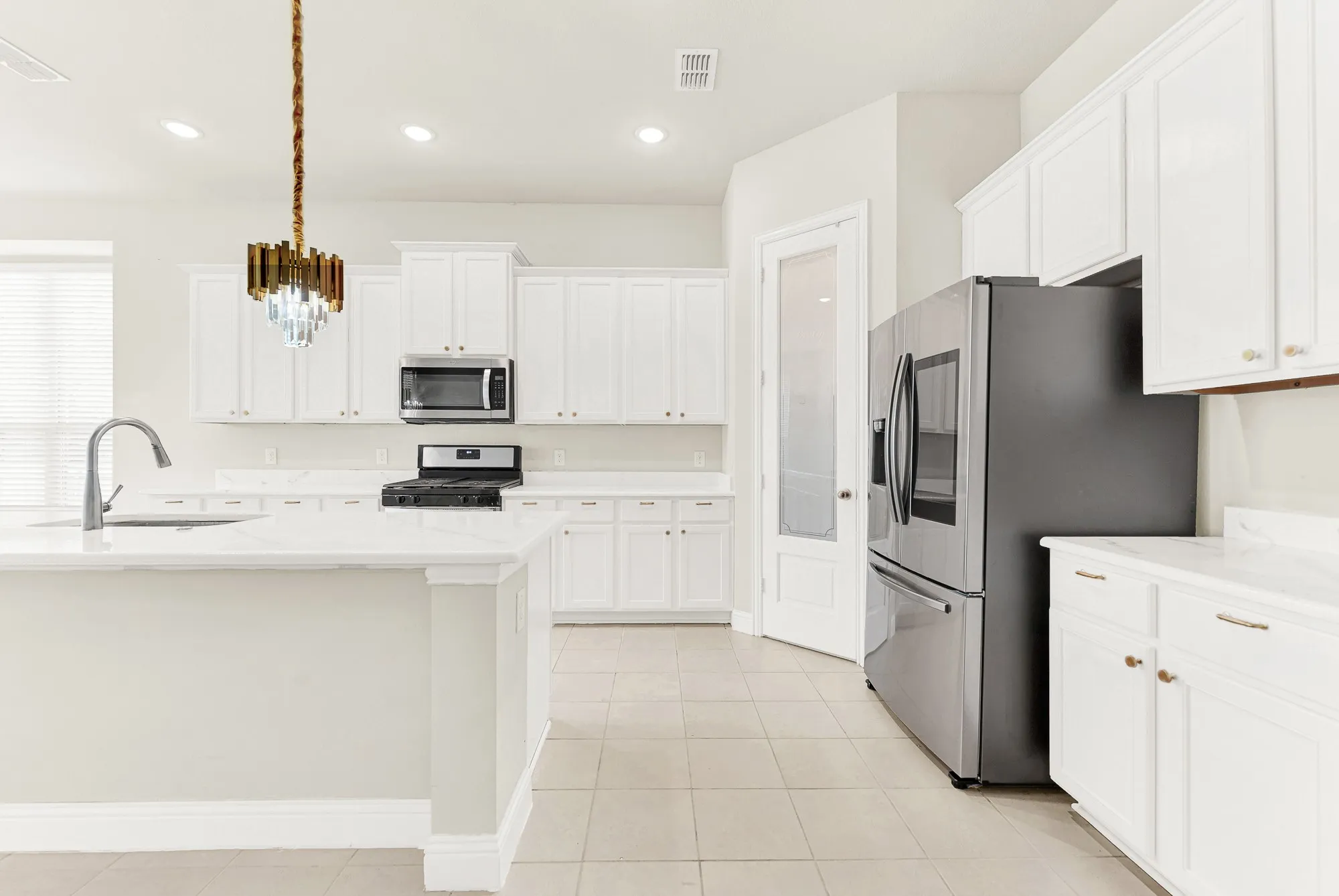Sleek stainless steel appliances are set against seamless white cabinetry and an frosted glass pantry door framed by tile flooring. It is easy to envision putting together a quick weeknight dinner while grabbing fresh ingredients right from the walk-in pantry.