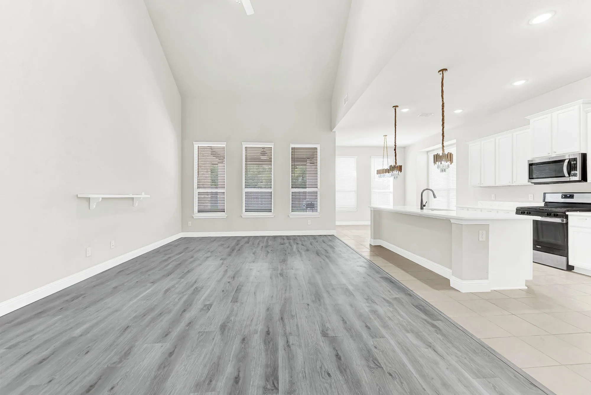 A trio of tall, framed windows floods the expansive living space with natural daylight while seamlessly connecting the room to the adjacent kitchen. Envision hosting lively game nights with family and friends where conversations effortlessly flow across the open floor plan.