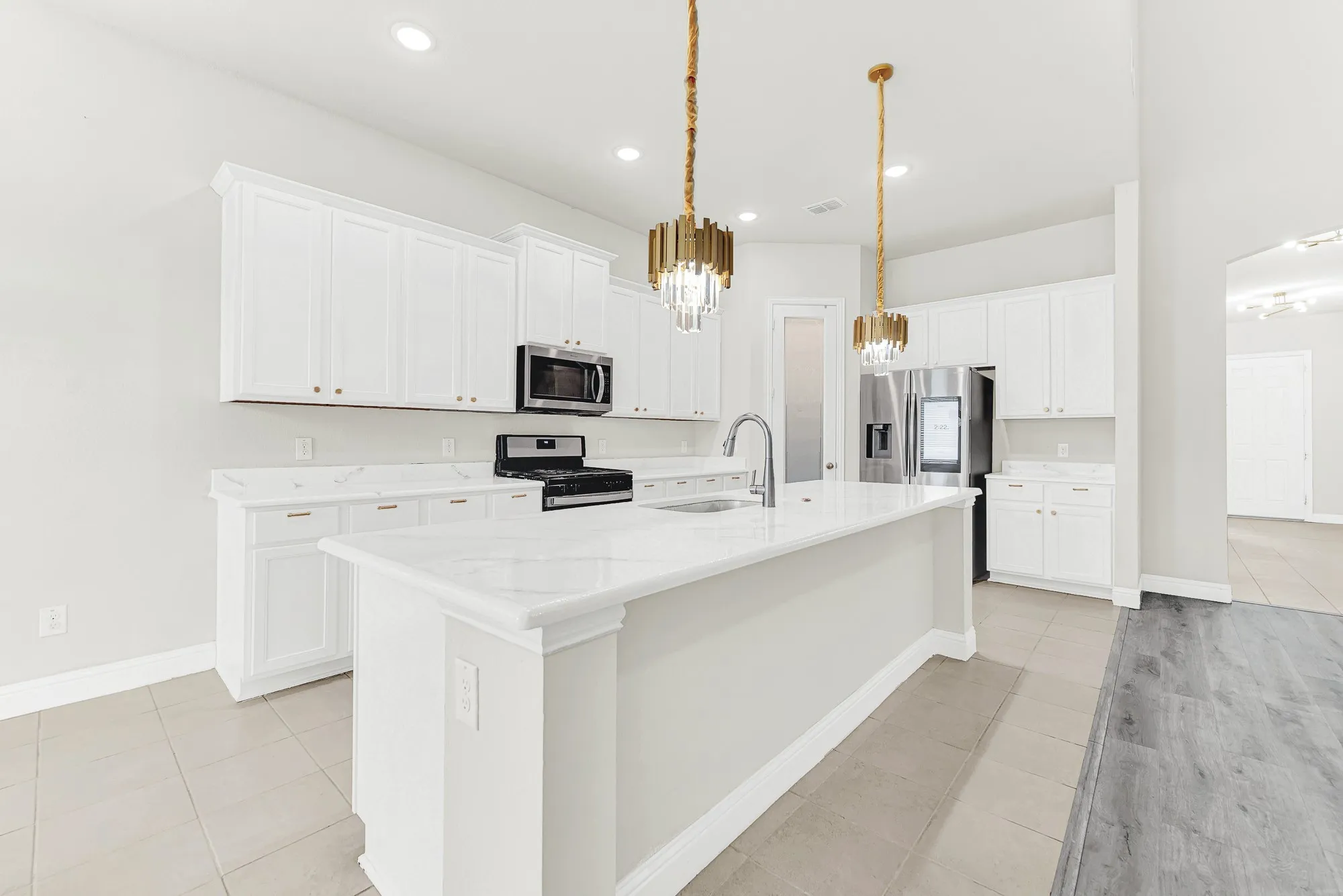 Polished quartz prep surfaces bounce gentle recessed lighting off clean white cabinetry and warm gold fixtures. picture whipping up fresh weekend pancakes with plenty of elbow room to spare on the generous island.
