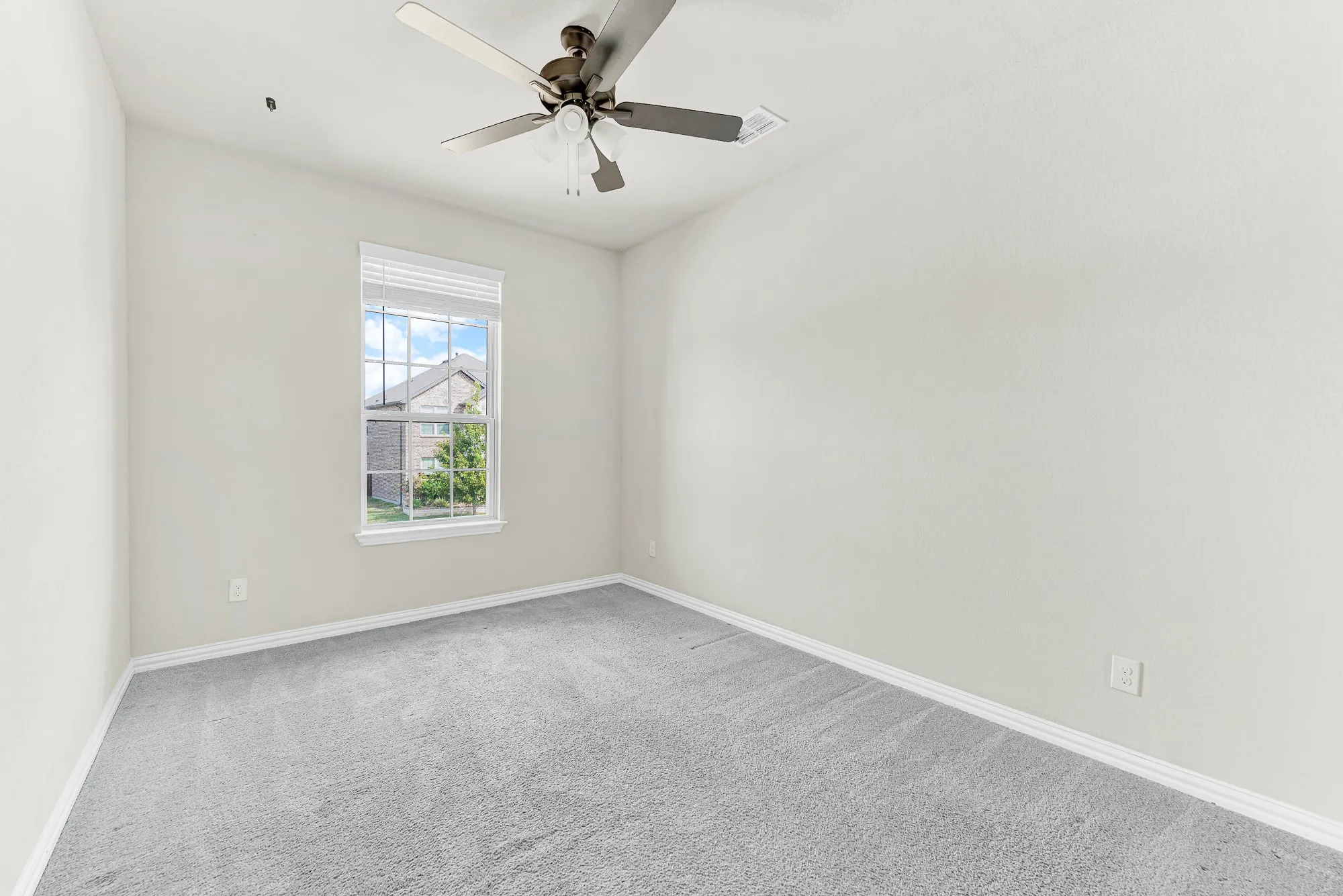 A single tall grid window filters gentle daylight into a quiet, cozy room anchored by a dark blade ceiling fan. Envision setting up a calm, sun-dappled nursery or dedicated creative studio away from the main living spaces.