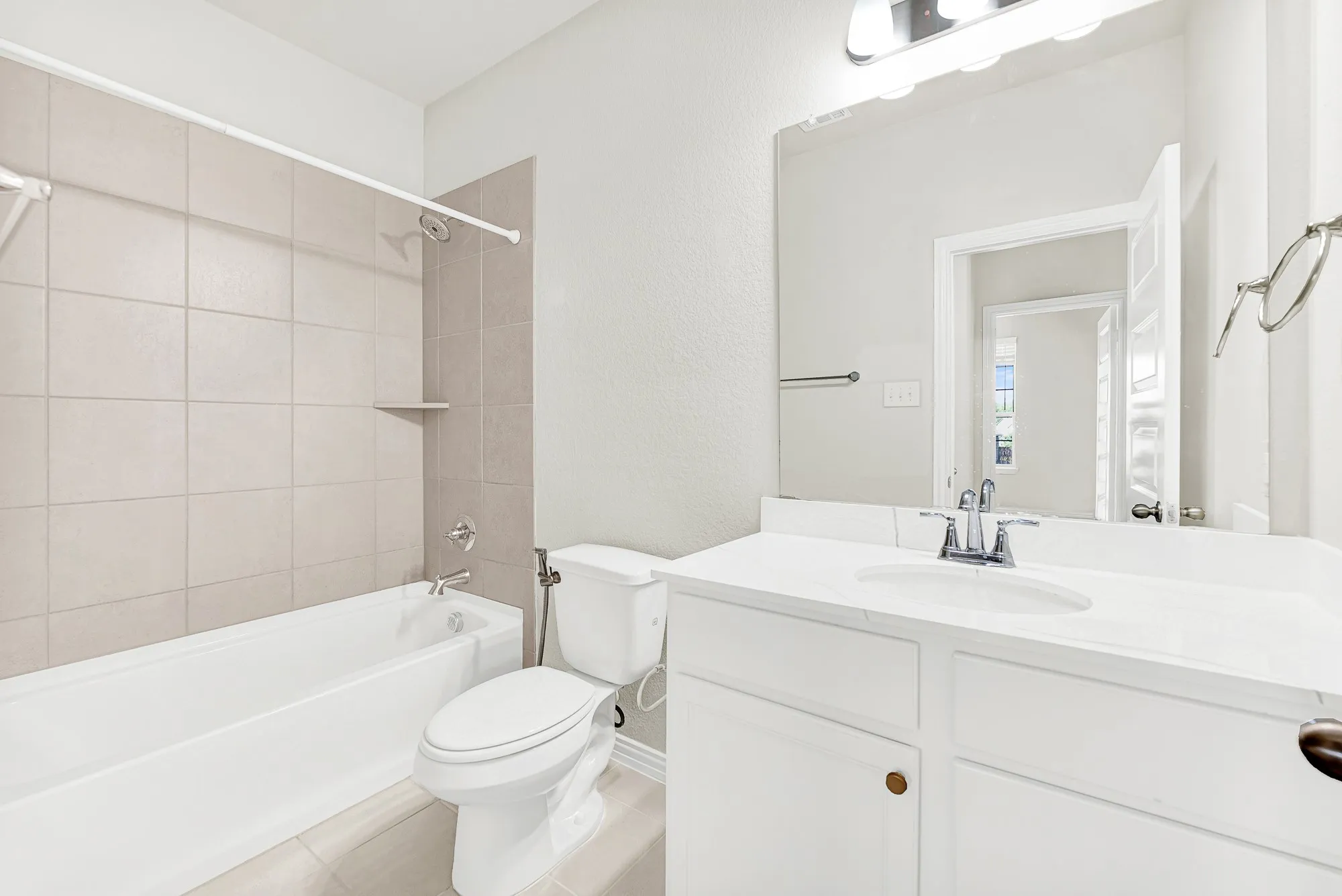 Neutral tiled tub surround pairs with a bright single vanity topped by a crisp illuminated mirror. Imagine guests enjoying a refreshing morning shower in a clean, private space tailored for effortless comfort.