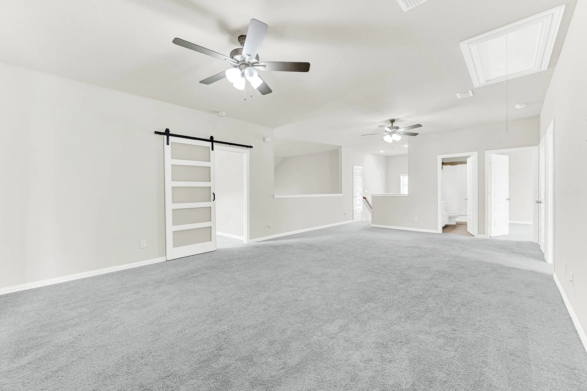 A sliding glass-paneled barn door adds modern character to a wide carpeted layout cooled by dual ceiling fans. You can easily picture setting up a pool table or media lounge where family members can gather for relaxed weekend fun.