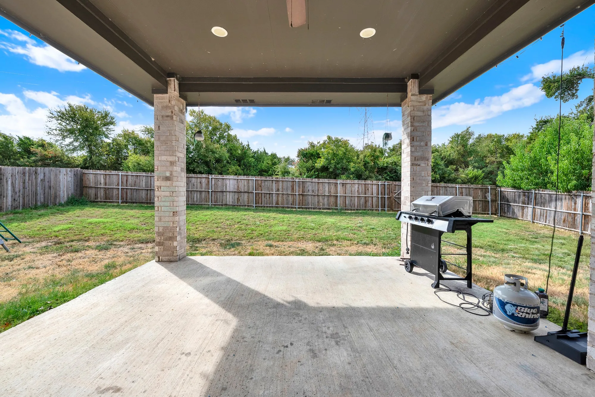A shaded concrete covered patio equipped with recessed ceiling lights and brick support pillars opens directly to green grass. You can easily see yourself grilling steaks for dinner while enjoying cool evening breezes on the patio.