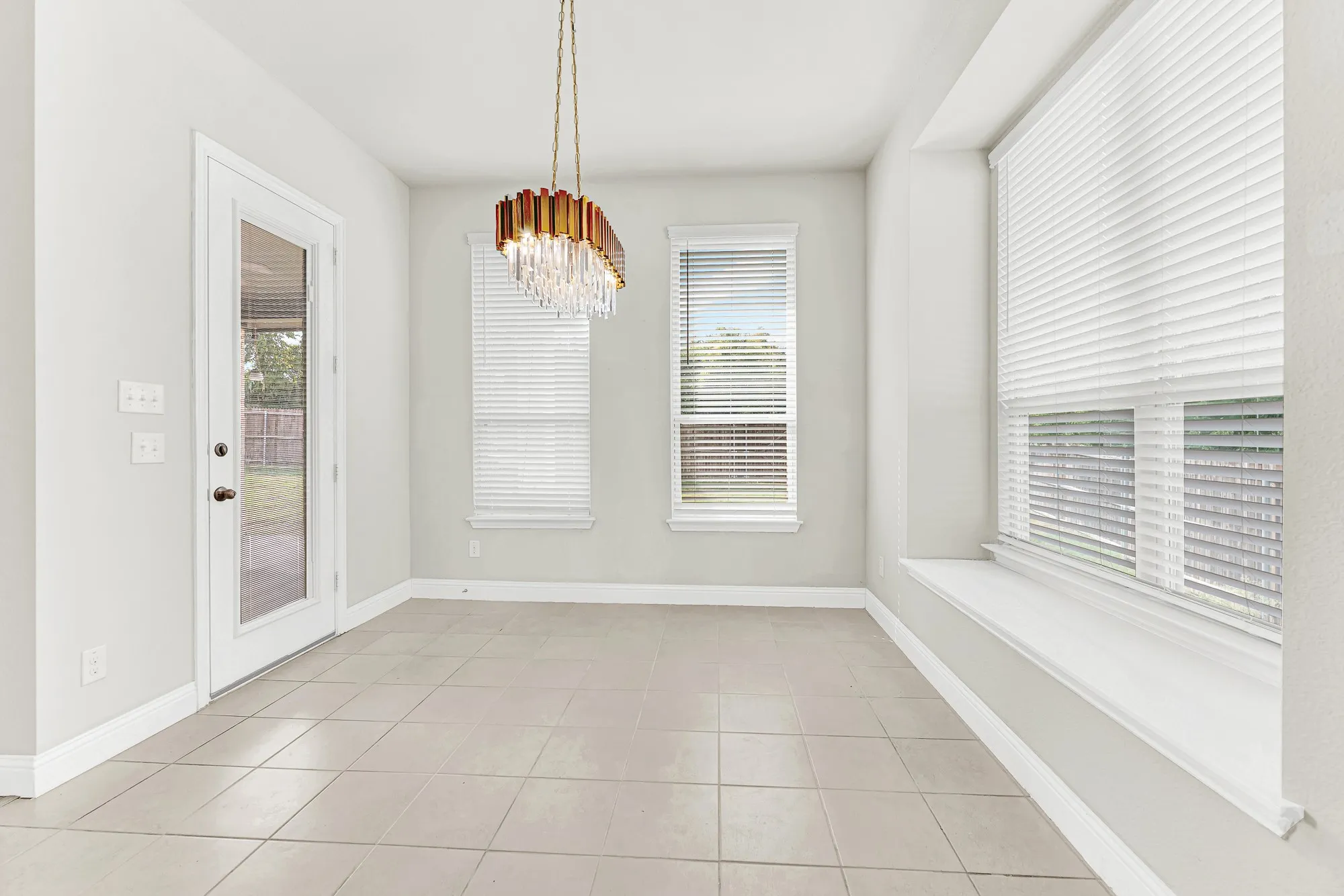 A deep bay window ledge creates an inviting alcove framed by a dramatic crystal and brass light fixture. Picture curling up on a custom cushion with a favorite book as warm daylight filters through the blinds.