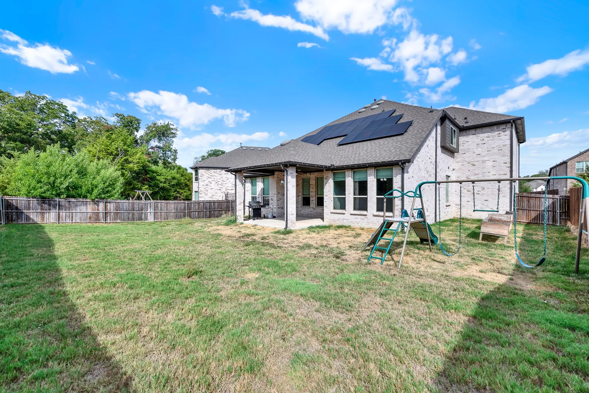 Energy-efficient rooftop solar panels top the rear elevation above a spacious, green yard bounded by a wooden privacy fence. Envision hosting summer barbecues where guests can freely stretch out and enjoy outdoor lawn games.