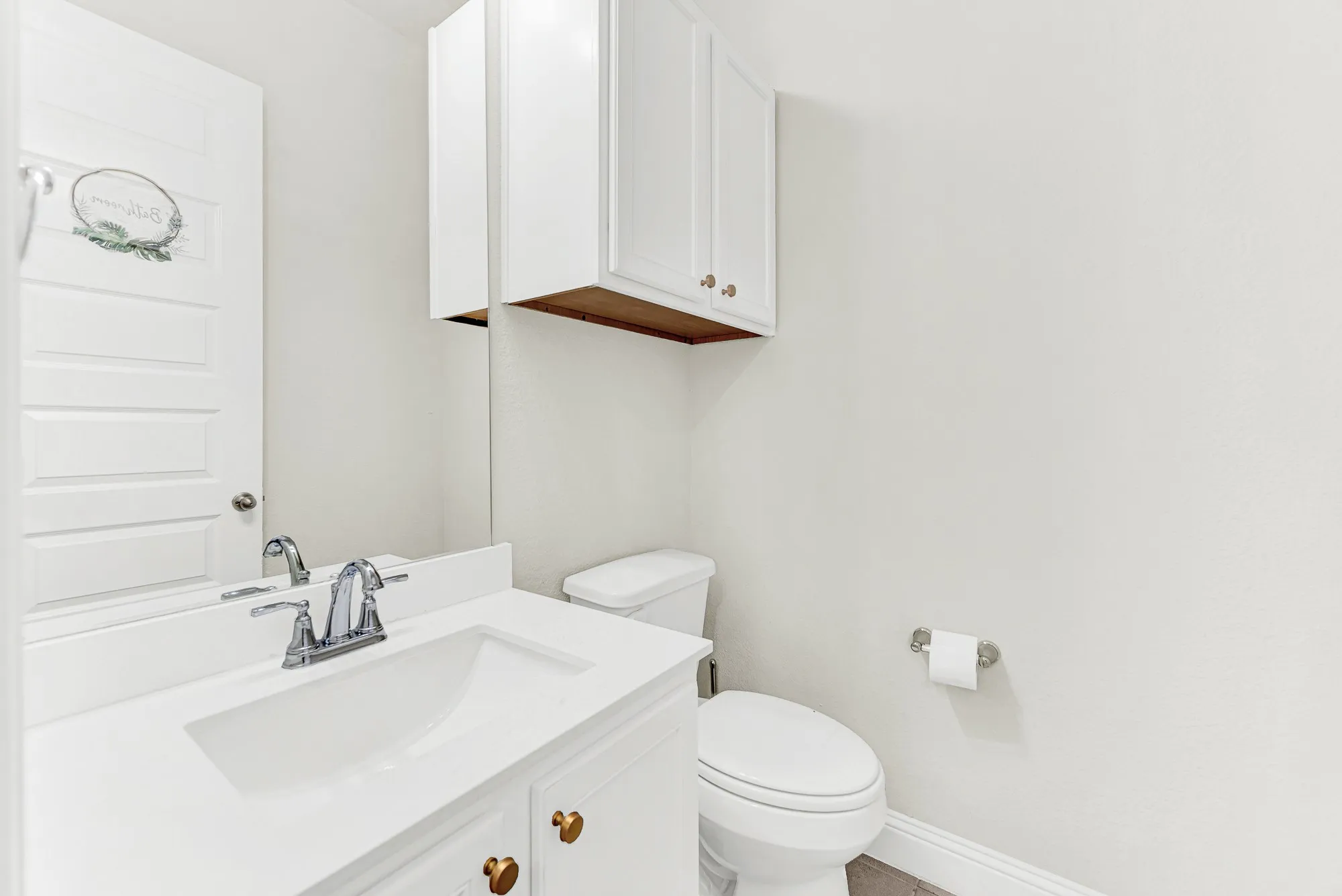 A crisp white vanity and matching wall cabinet pair with warm brass hardware to maximize vertical space in a clean powder room layout. Picture guests freshening up in a quiet, cozy space thoughtfully tailored for effortless entertaining.