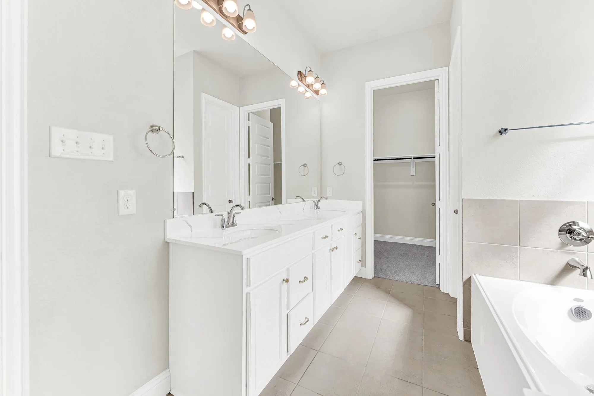 An expansive dual-sink vanity with bright vanity lighting offers abundant counter space that leads directly into a large walk-in closet. Picture getting ready for a night out with plenty of elbow room and seamless organization at your fingertips.