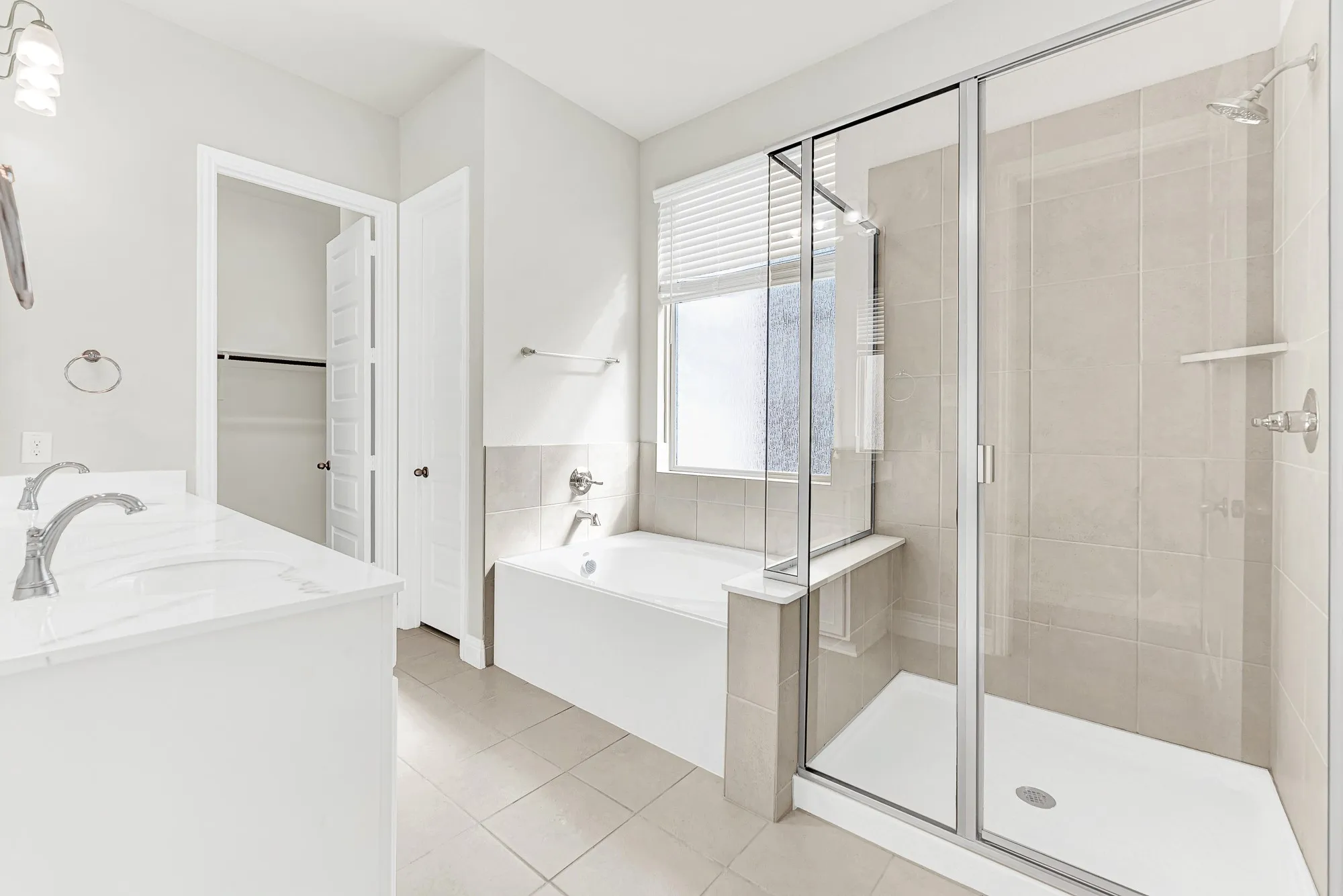 A deep soaking tub sits beneath a frosted privacy window next to a glass-enclosed walk-in shower lined with warm neutral tile. Envision taking a long, relaxing bubble bath to wash away stress at the end of the week.