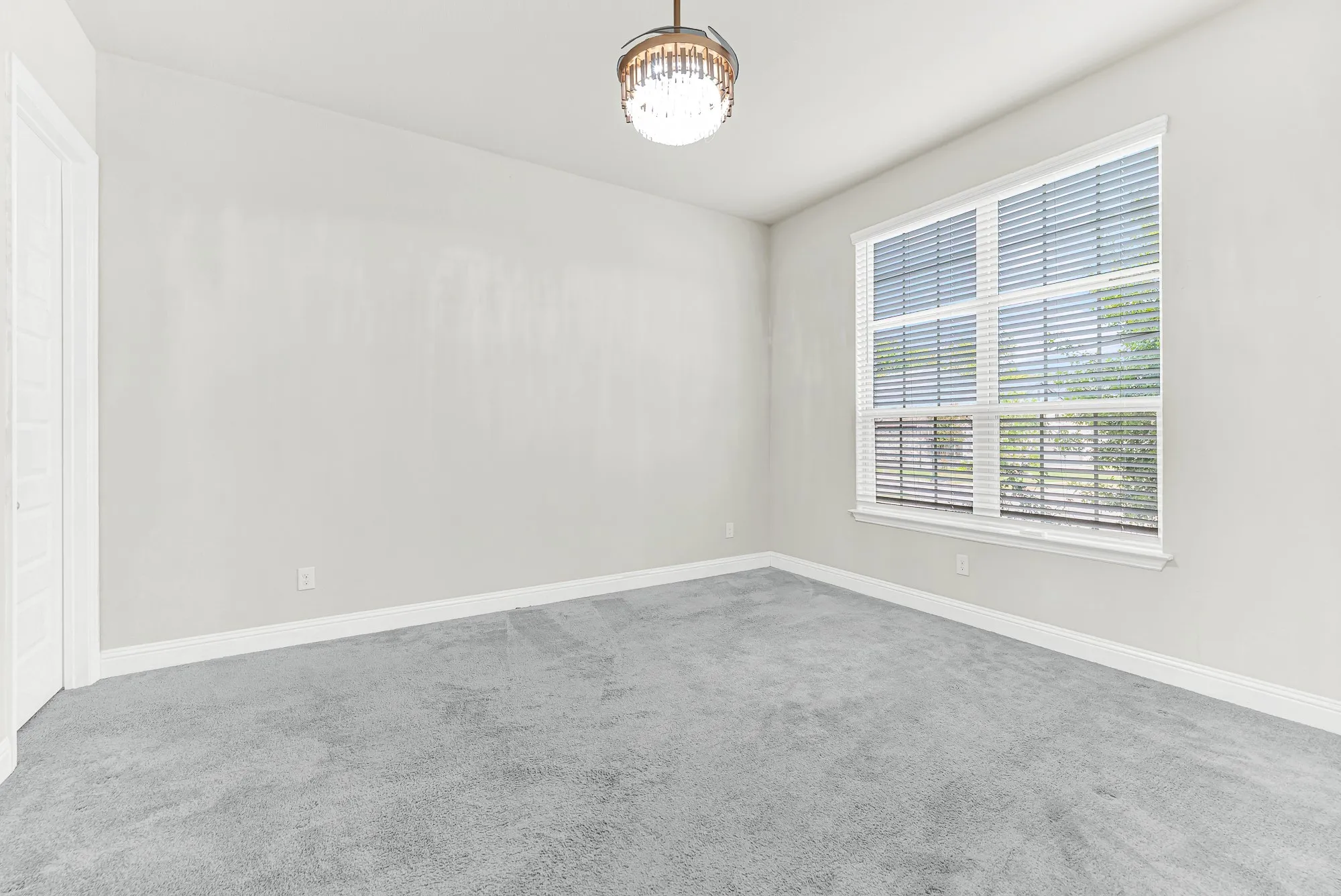 A large multi-pane window bathes plush carpeted floors in soft morning sunlight beneath an elegant crystal fandelier. Picture enjoying a quiet morning with fresh coffee in hand as natural light brightens your work space.