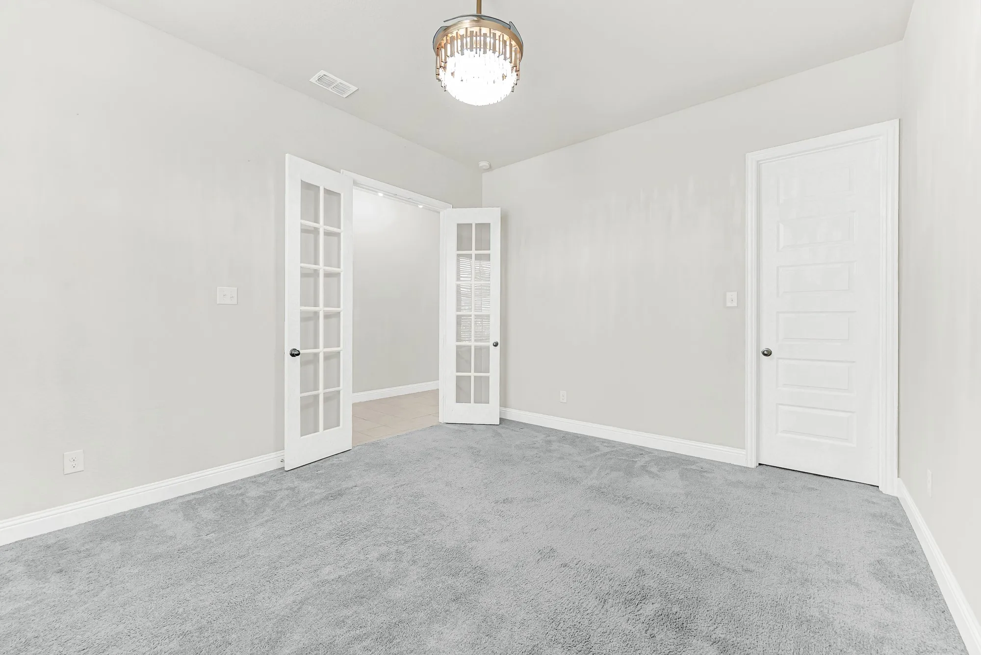 Classic glass French doors open into a private, quiet retreat featuring smooth neutral walls and plush underfoot comfort. It is easy to visualize focusing on creative projects or taking quiet afternoon calls with complete privacy.
