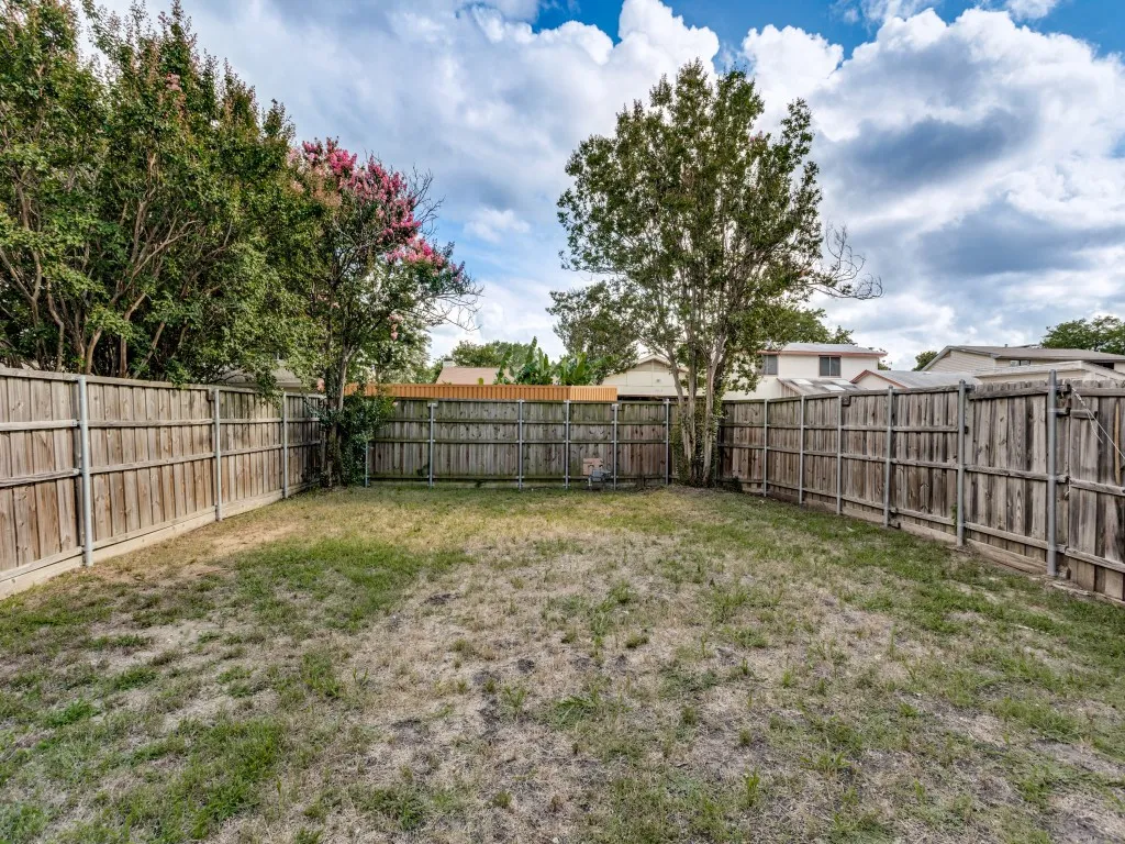 Enclosed backyard featuring wood fencing, mature trees, and a grass lawn
