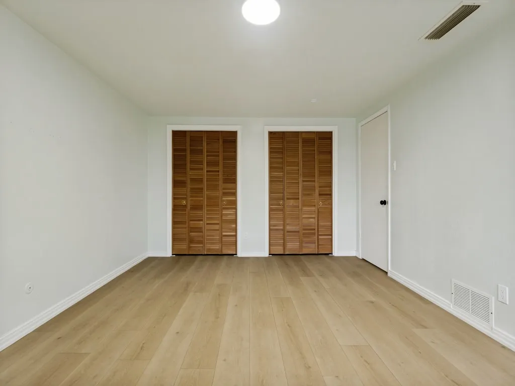 Light wood-finish flooring, two sets of louvered bifold closet doors, and white walls