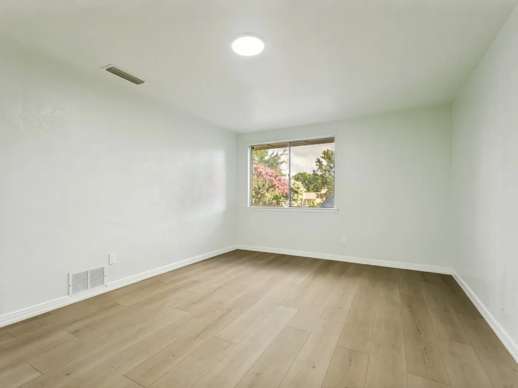Wood-finish flooring, white baseboards, window with exterior scenery, ceiling-mounted light fixture, and white wall finishes