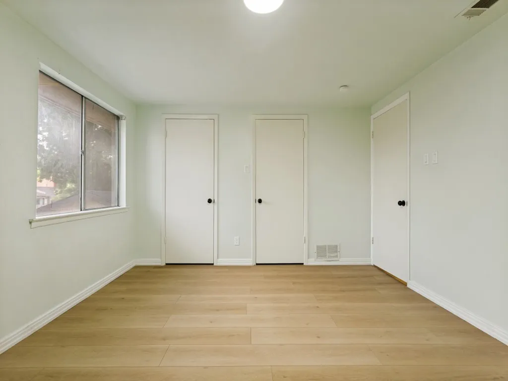 Wood-finish flooring, multiple white doors, and a window with a white frame