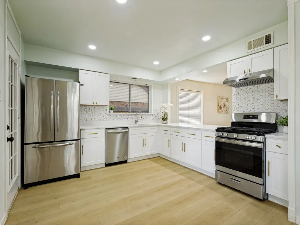 Full kitchen with white cabinetry, stainless steel appliances, patterned tile backsplash, light-toned wood-finish flooring, and recessed lighting