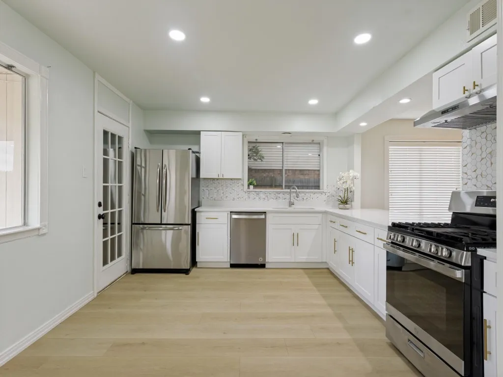 White cabinetry with gold-tone hardware, stainless steel appliances, wood-finish flooring, and recessed ceiling lighting
