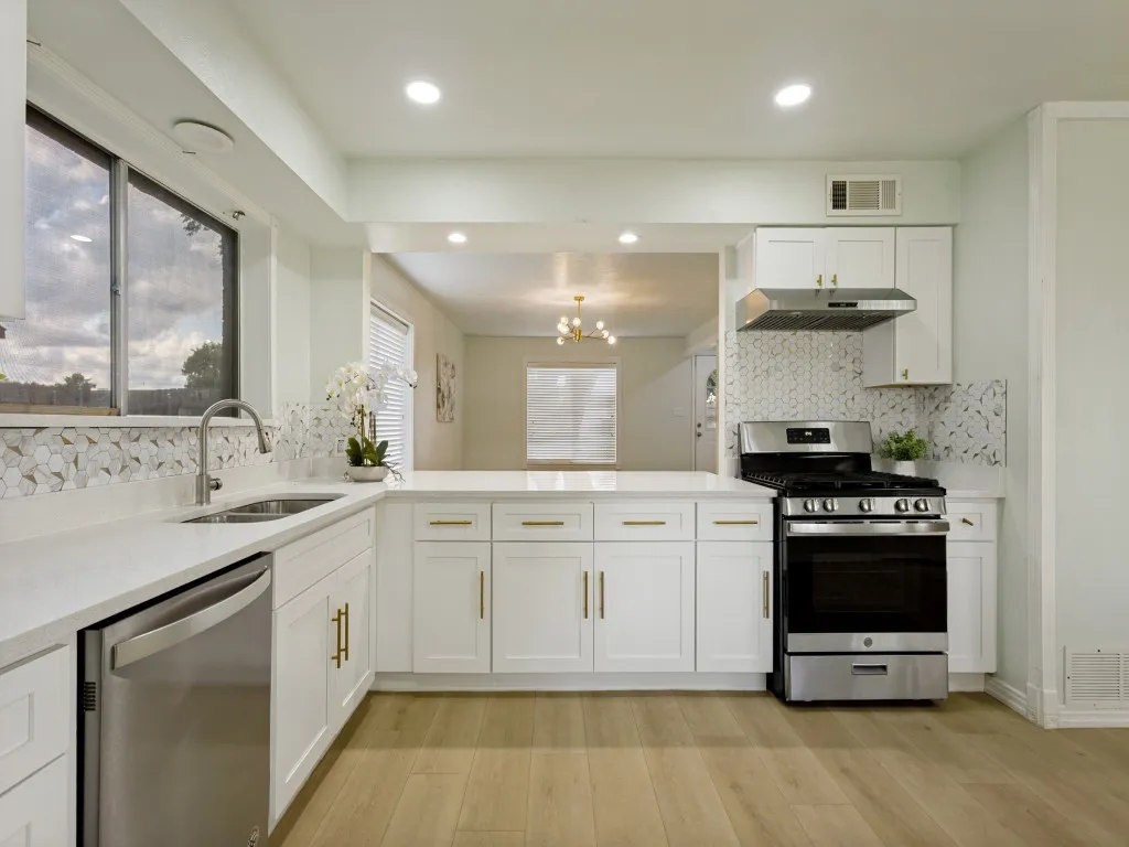 White cabinetry with gold-tone hardware, white countertops, stainless steel appliances, and a mosaic tile backsplash