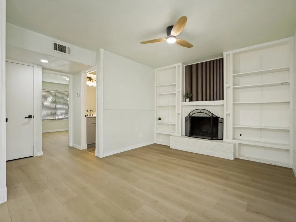 Wood-finish flooring throughout, fireplace with a decorative screen, built-in shelving, and a ceiling fan with integrated lighting
