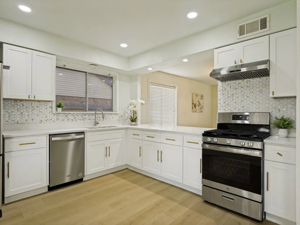 Kitchen featuring white cabinetry, stainless steel appliances, quartz countertops, a patterned tile backsplash, and wood-finish flooring