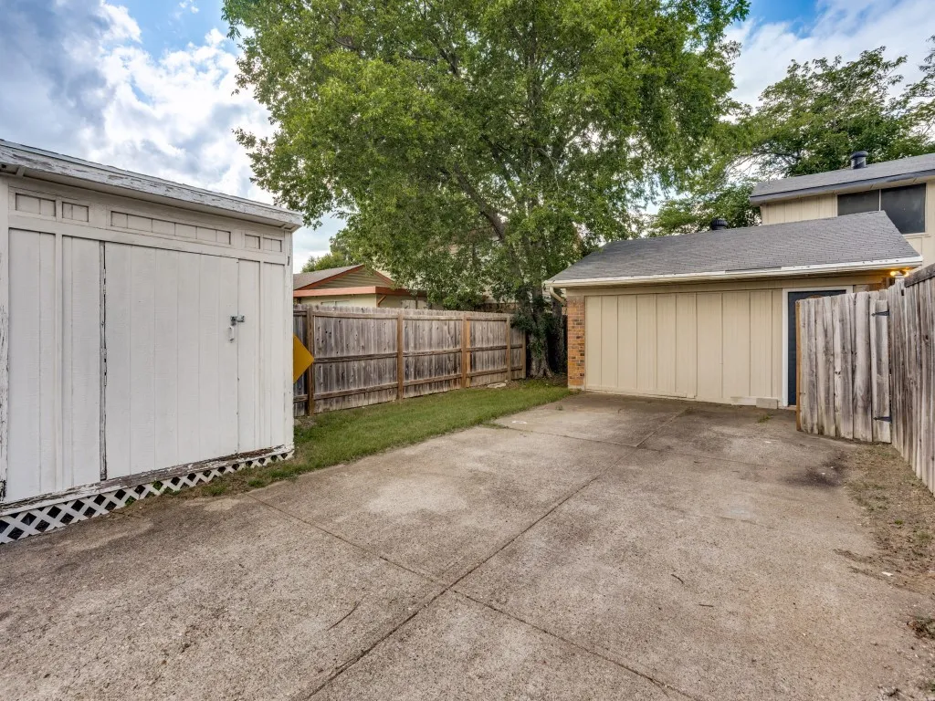 Detached storage shed, wood privacy fencing, concrete driveway, attached garage, and mature trees