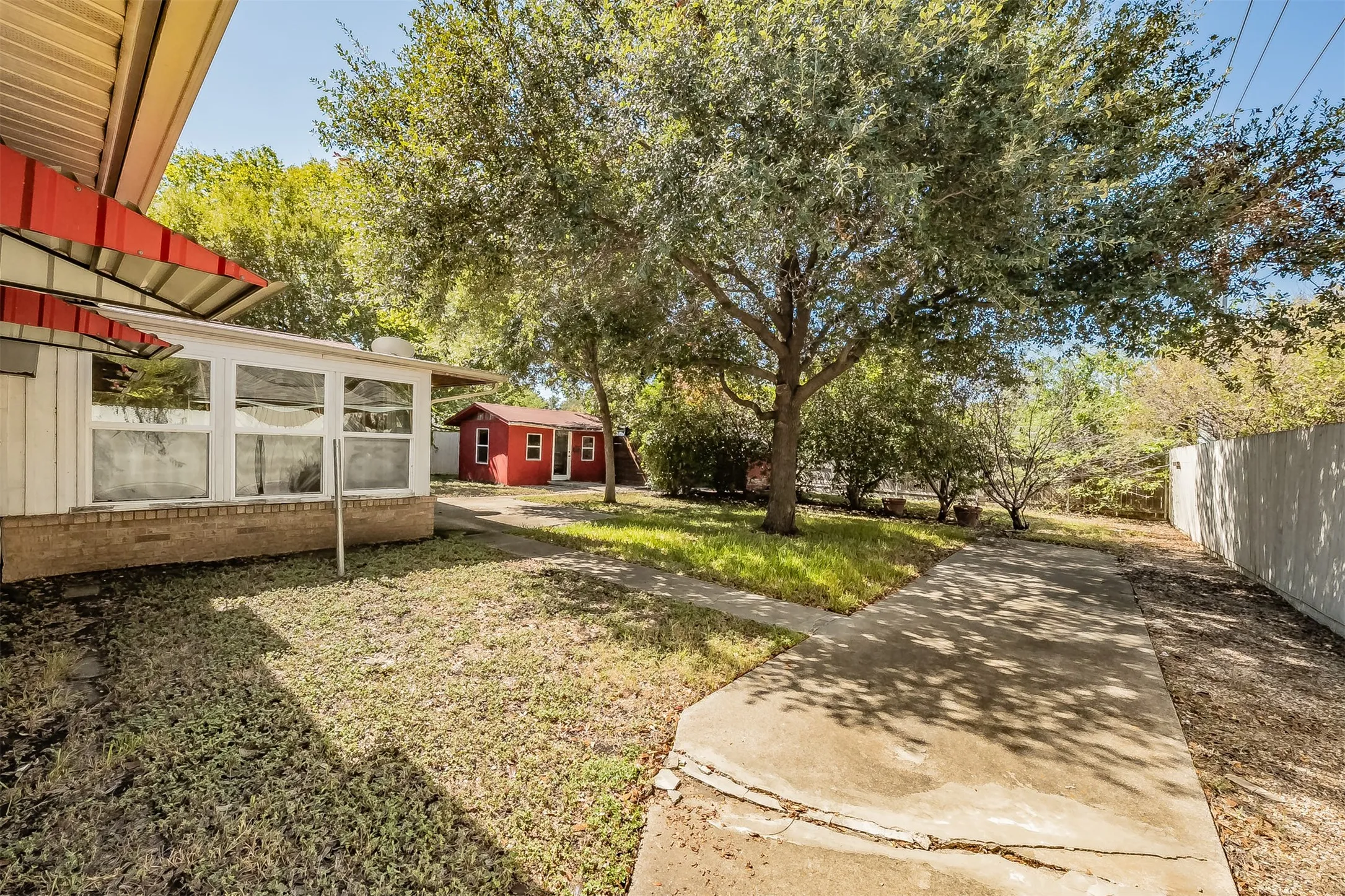 Sunroom addition with multiple windows, concrete walkway, mature trees, and a detached red storage shed