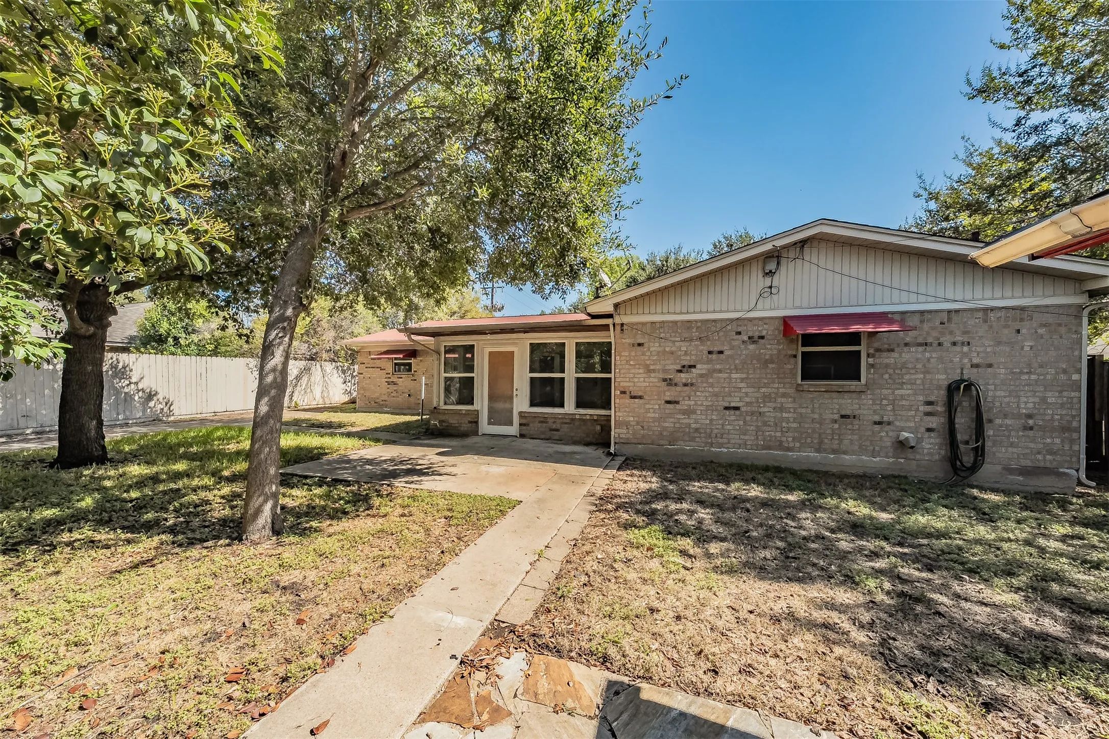 Back exterior featuring brick siding, multiple windows, a screened door, and a concrete pathway