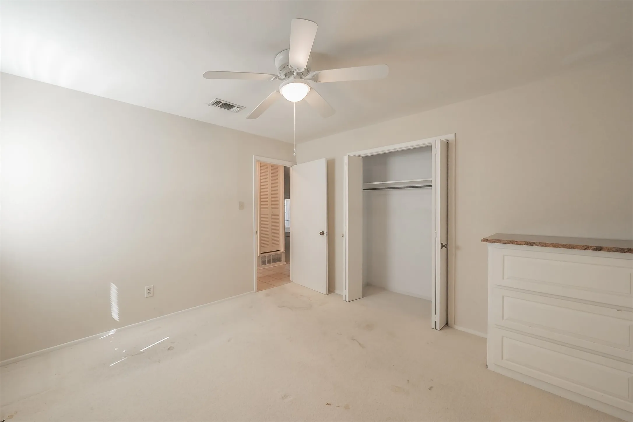 Recessed ceiling fan with integrated lighting, carpeted flooring, built-in dresser with stone-finish countertop, and bi-fold closet doors