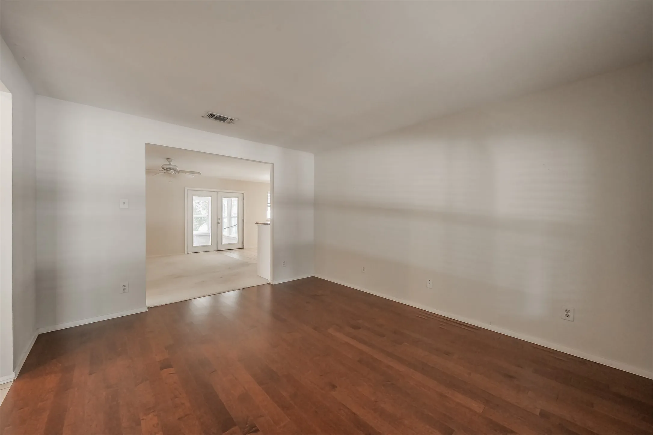 Hardwood flooring, white painted walls, and an open architectural feature leading to an additional space with French doors and carpeted flooring