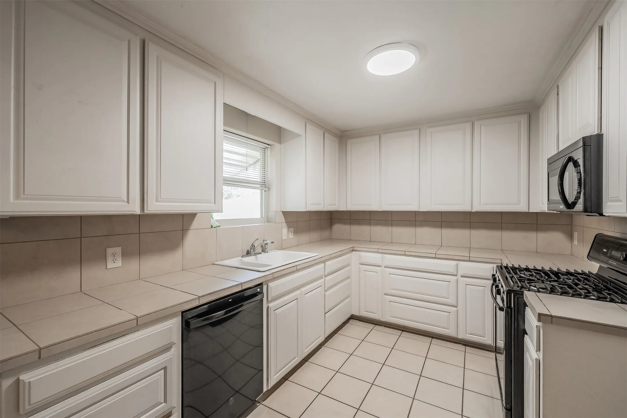 White cabinetry, tile flooring, tile countertops, recessed lighting, and a built-in microwave