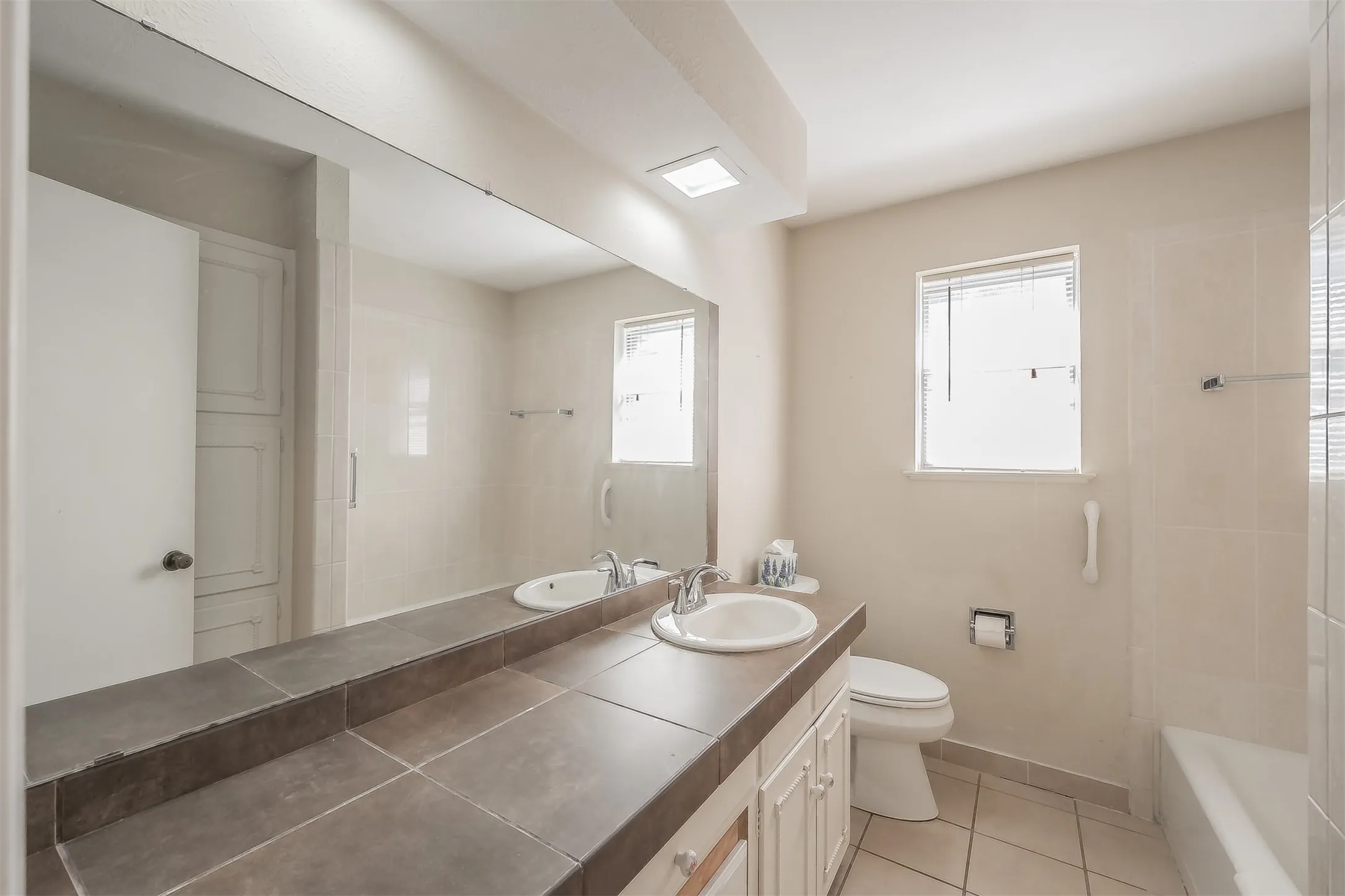 Bathroom featuring a full-width vanity mirror, tile countertop, white cabinetry, an integrated sink, and a built-in storage cabinet