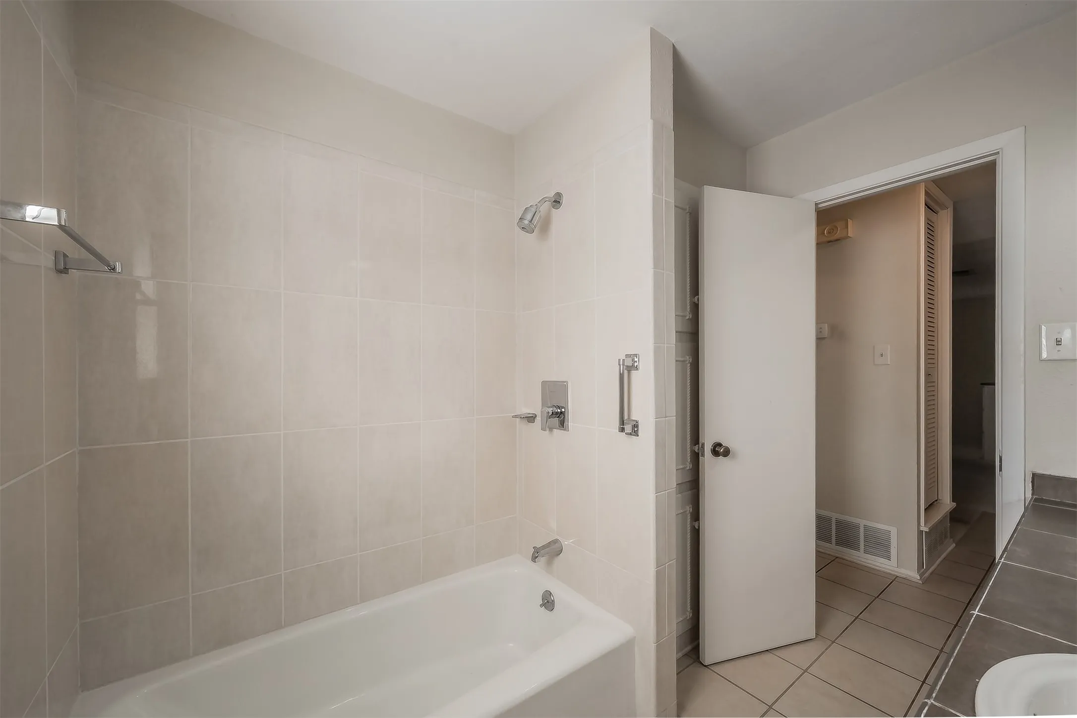 Bathtub with tiled surround, chrome shower fixtures, and a white vanity with a rectangular sink