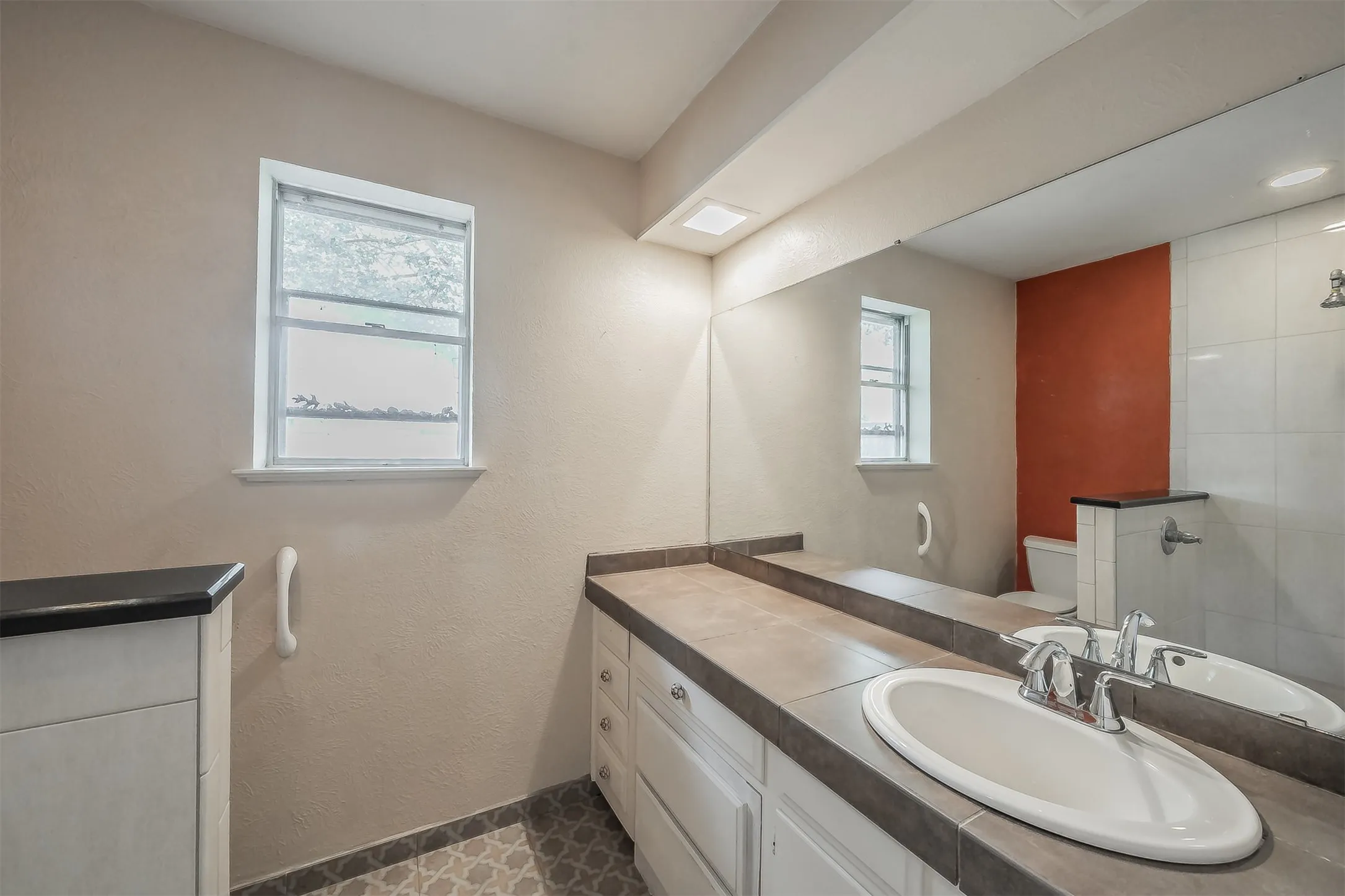 Bathroom featuring a window, patterned floor tile, white vanity cabinetry, a built-in sink with chrome faucet, and a large wall-mounted mirror