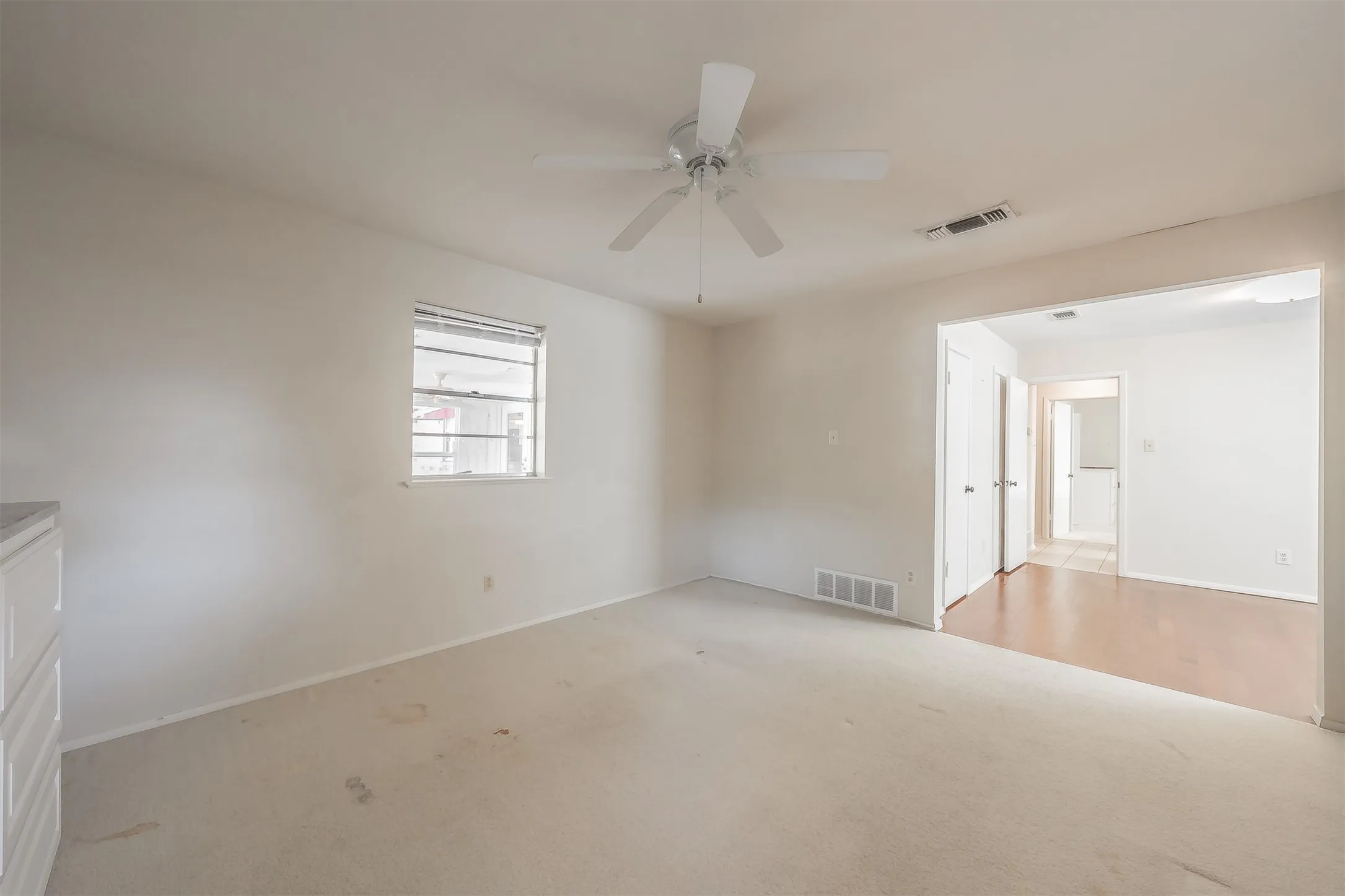 White ceiling fan with integrated lighting, window with horizontal blinds, and a built-in white dresser with cabinet doors and drawers