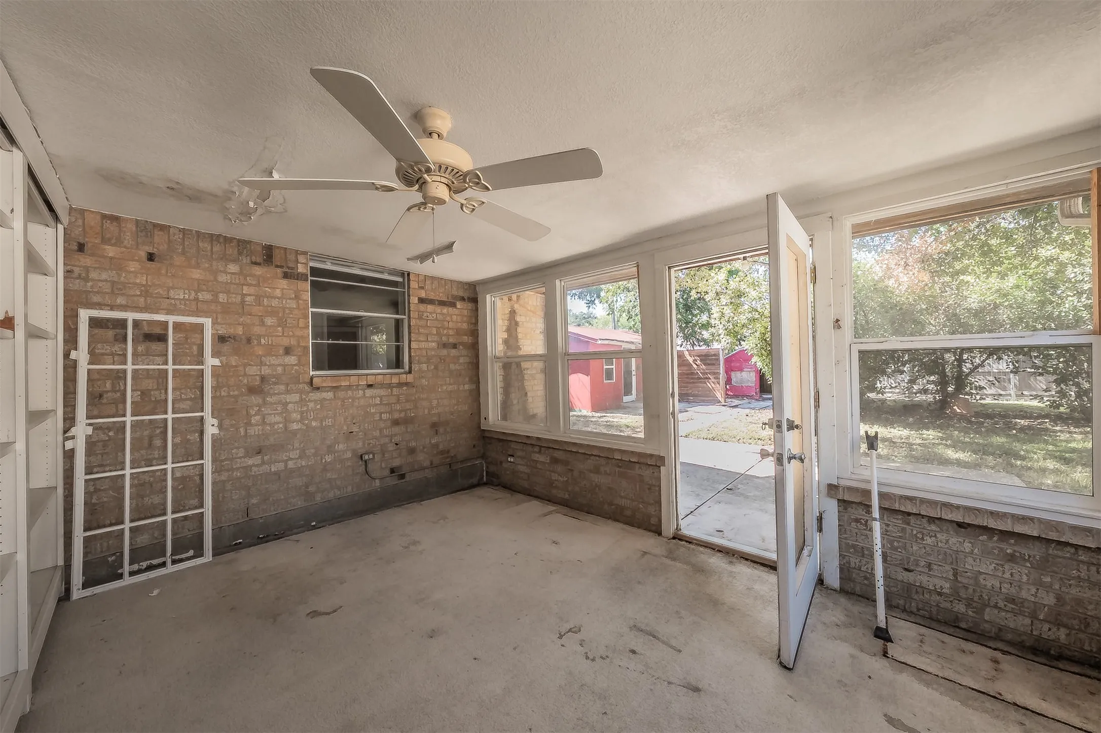 Sunroom featuring brick walls, concrete flooring, built-in shelving, a ceiling fan, and multiple windows