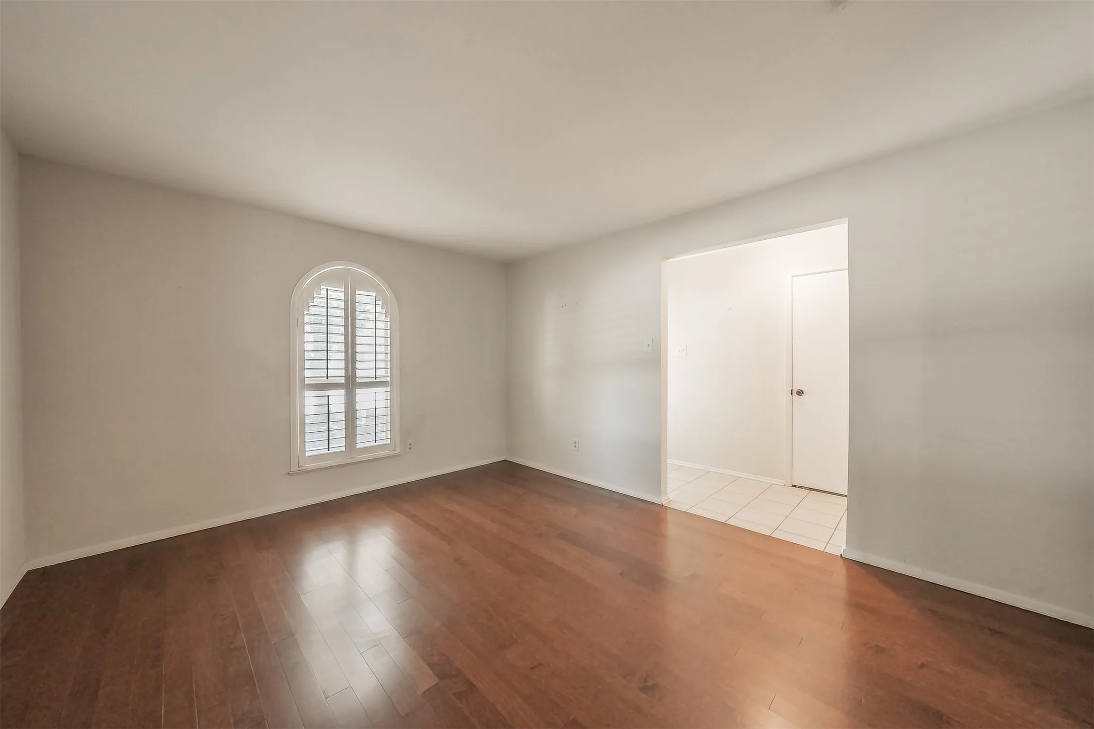 Wood-finish flooring, arched window with white plantation shutters, and a white interior door