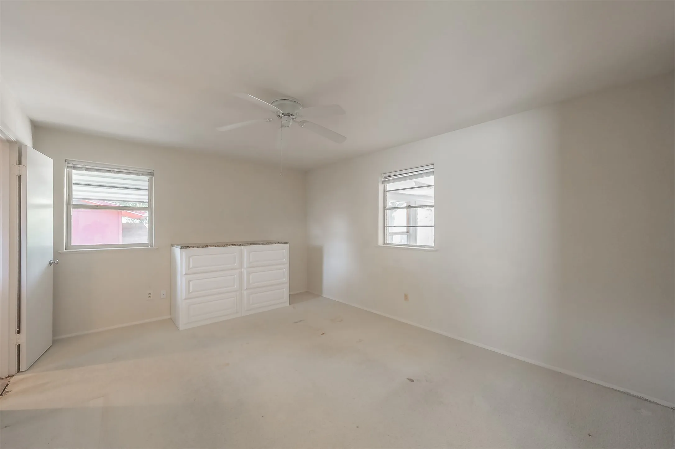 White walls with two windows, a ceiling fan, and a built-in dresser with a stone-finish countertop