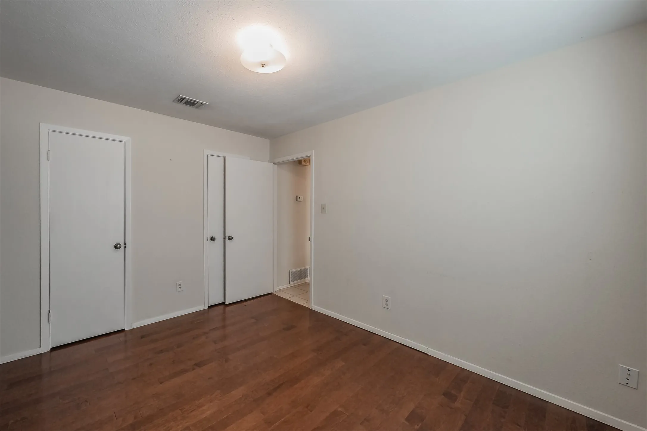 Wood-finish flooring with neutral wall tones and a flush-mount ceiling light
