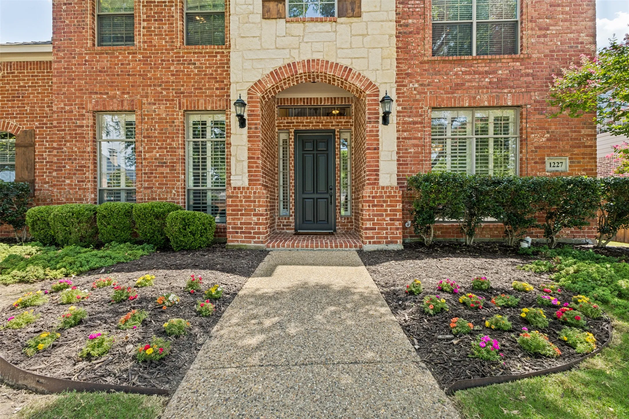 Brick and stone facade featuring an arched entryway with sconce lighting