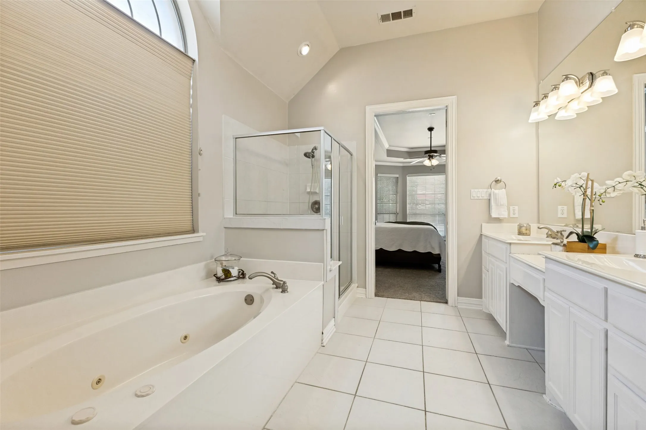 White tile flooring, dual vanities with integrated sinks, a built-in jetted tub, a glass-enclosed shower, and a vaulted ceiling