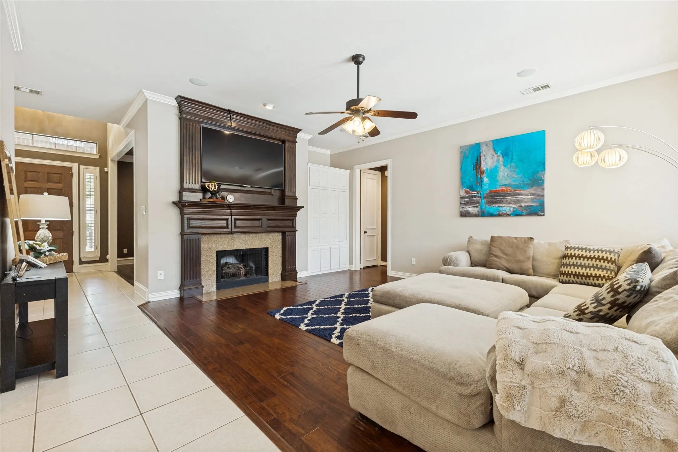 Living area featuring wood-finish flooring, a detailed fireplace with a stone surround and dark wood mantel, and a ceiling fan