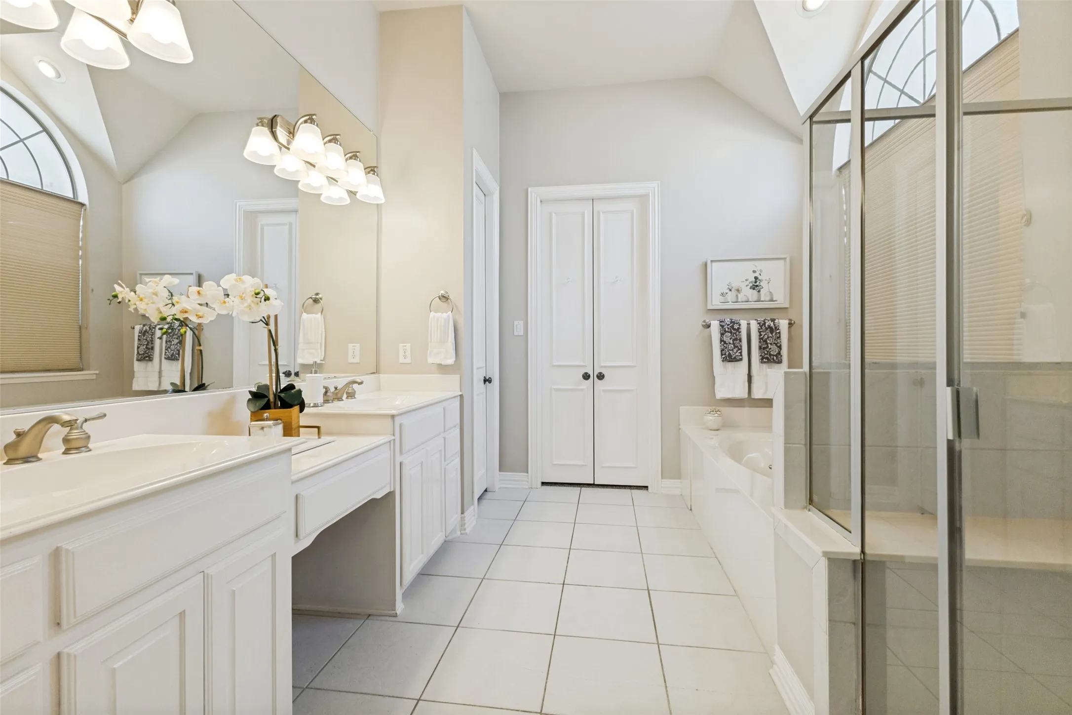 Spacious bathroom featuring dual vanities with integrated sinks, a built-in soaking tub, and a glass-enclosed shower