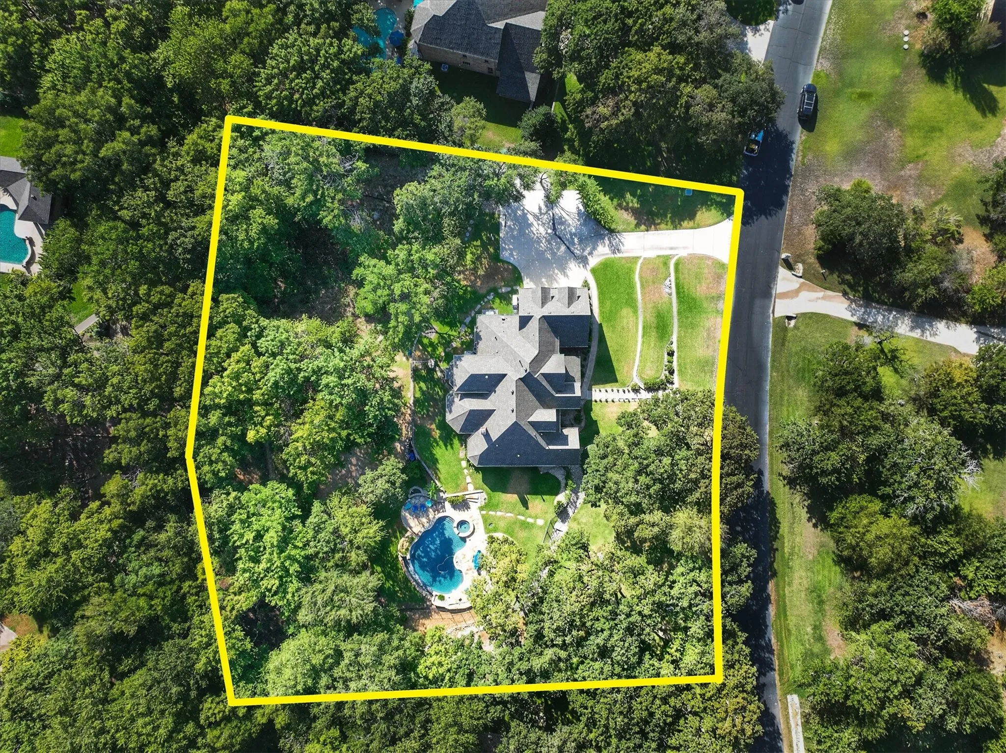 Expansive property featuring a multi-level roofline, extensive mature tree coverage, a curved driveway, and a custom-shaped swimming pool