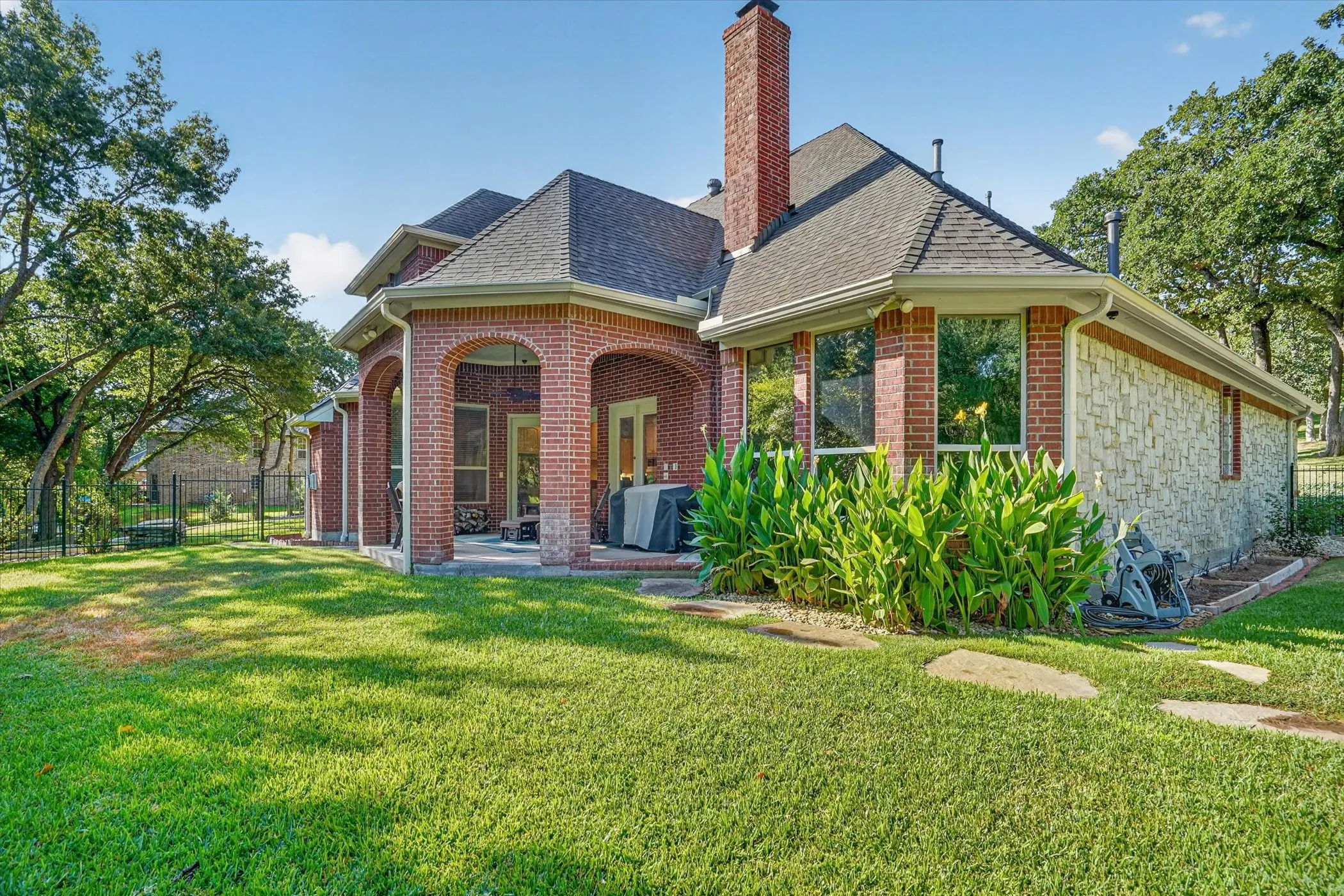 Brick and stone exterior with a covered patio, multiple windows, and a mature treeline