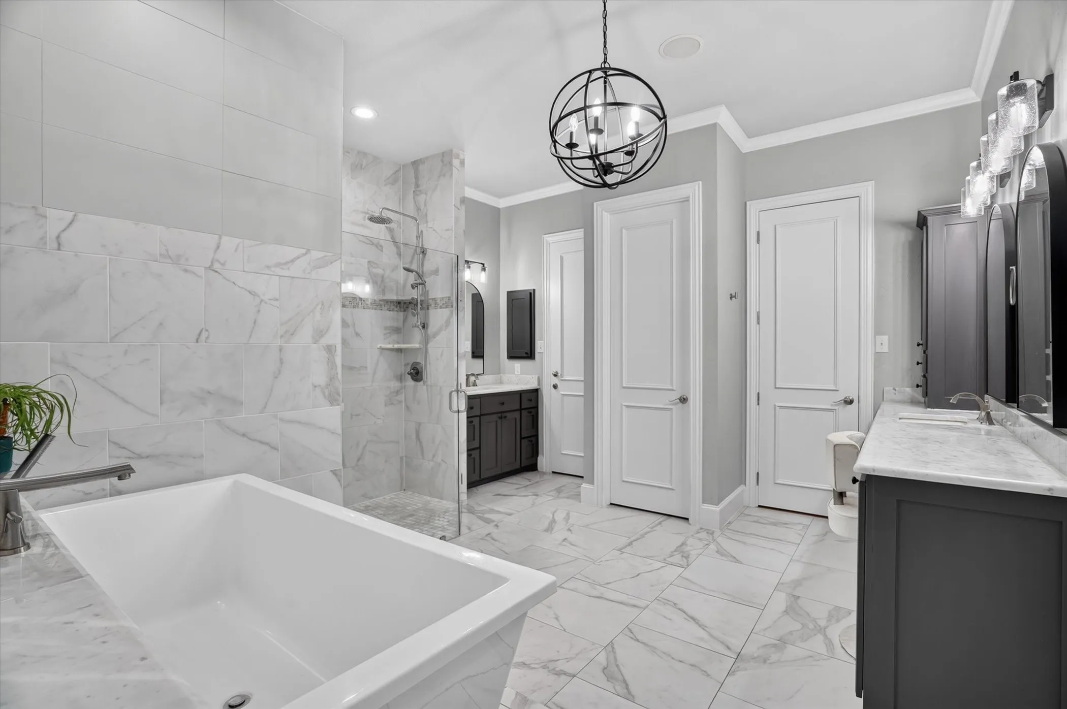 Freestanding bathtub glass-enclosed shower, dual vanities with dual sinks, and a spherical chandelier