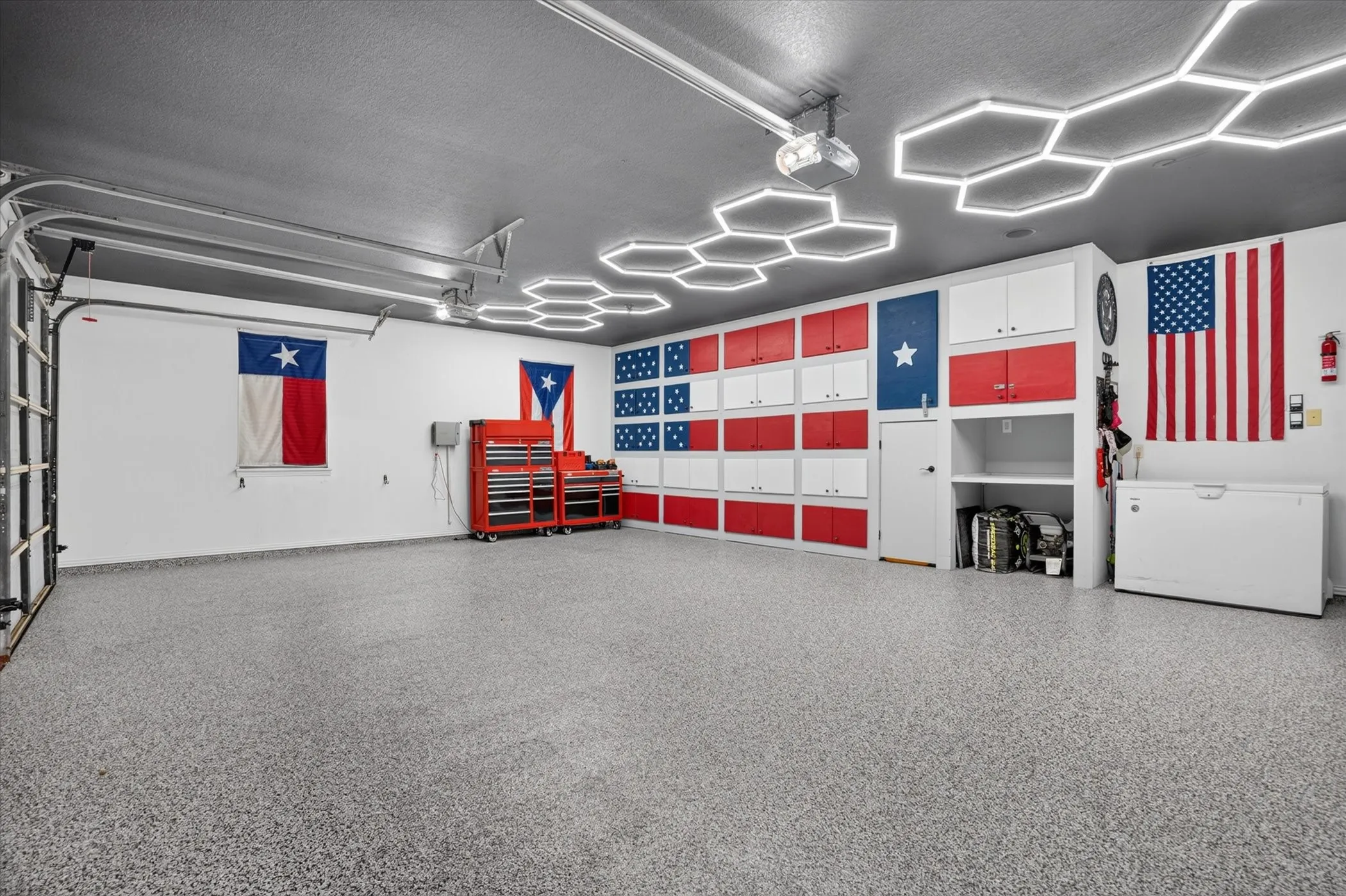 Epoxy-coated flooring, built-in cabinetry, overhead track lighting, hexagonal ceiling light fixtures, and an overhead garage door